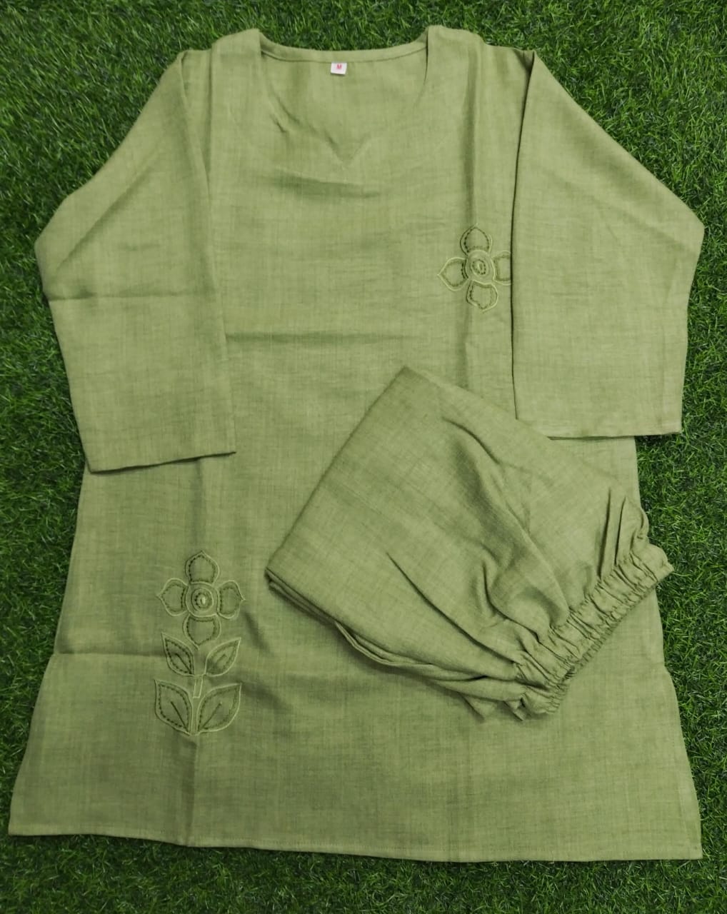 Green outfit with floral embroidery on a green grass background
