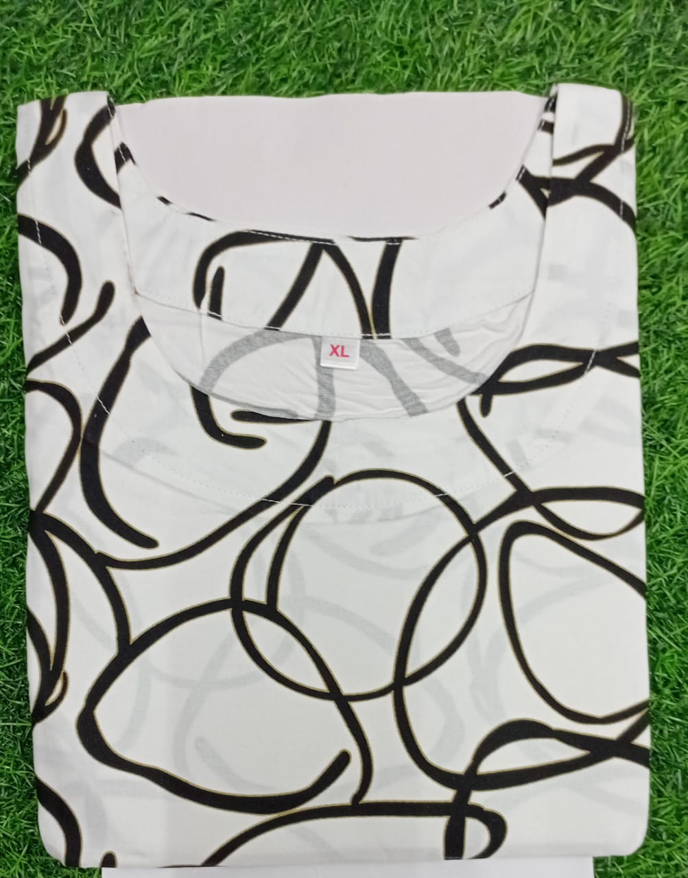 White tank top with black abstract pattern on grass