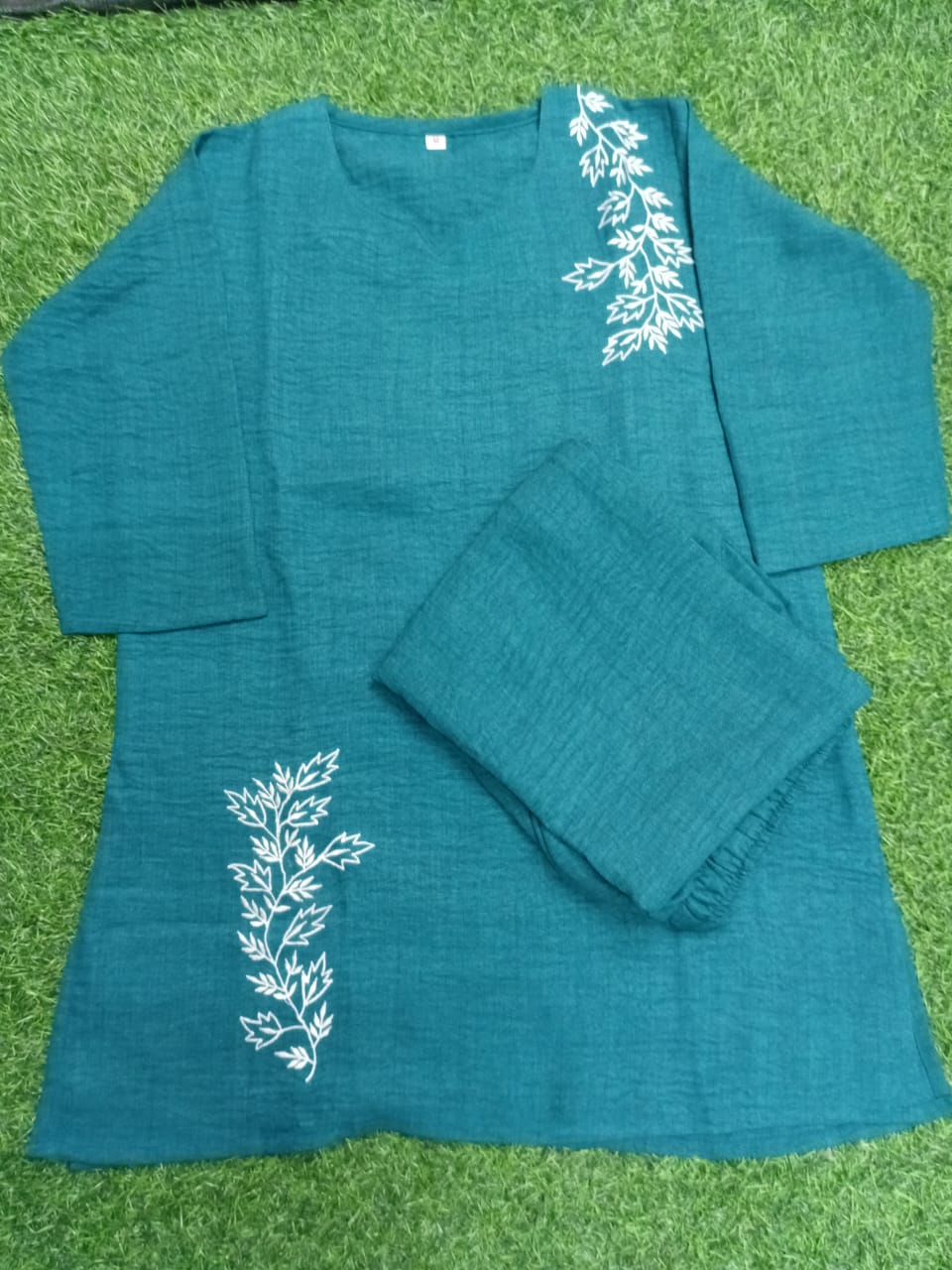 Teal outfit with white floral embroidery on a grass background