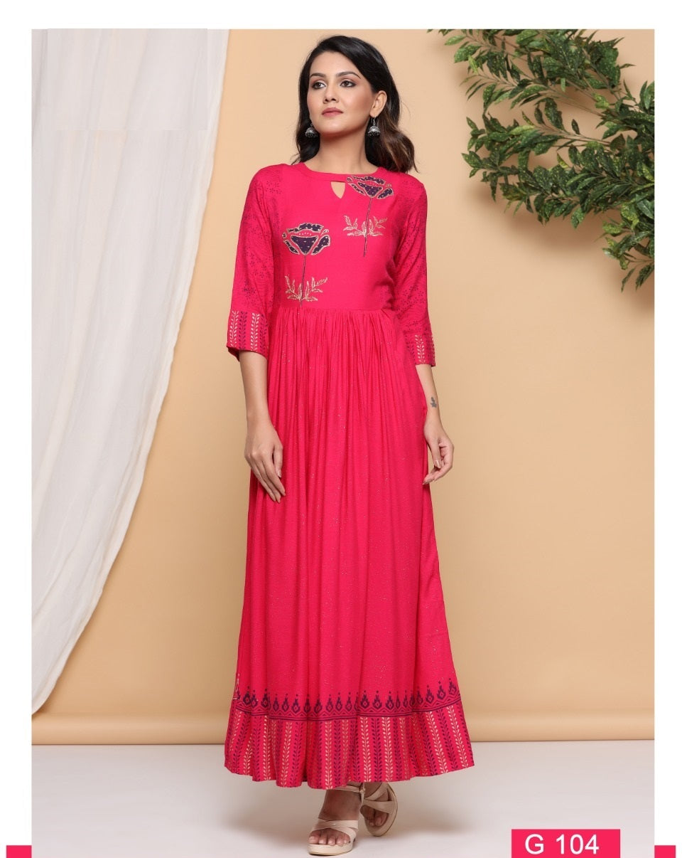 A woman wearing a dark pink A-line kurti with gold print and flared design, standing against a neutral backdrop.