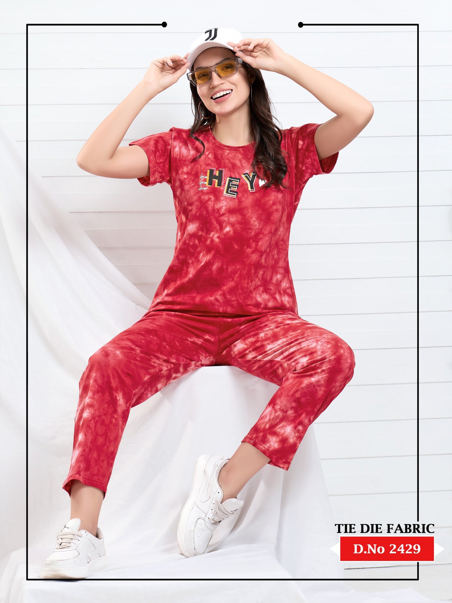 Person wearing a red tie-dye outfit with 'HEY' text, sitting on a white surface.