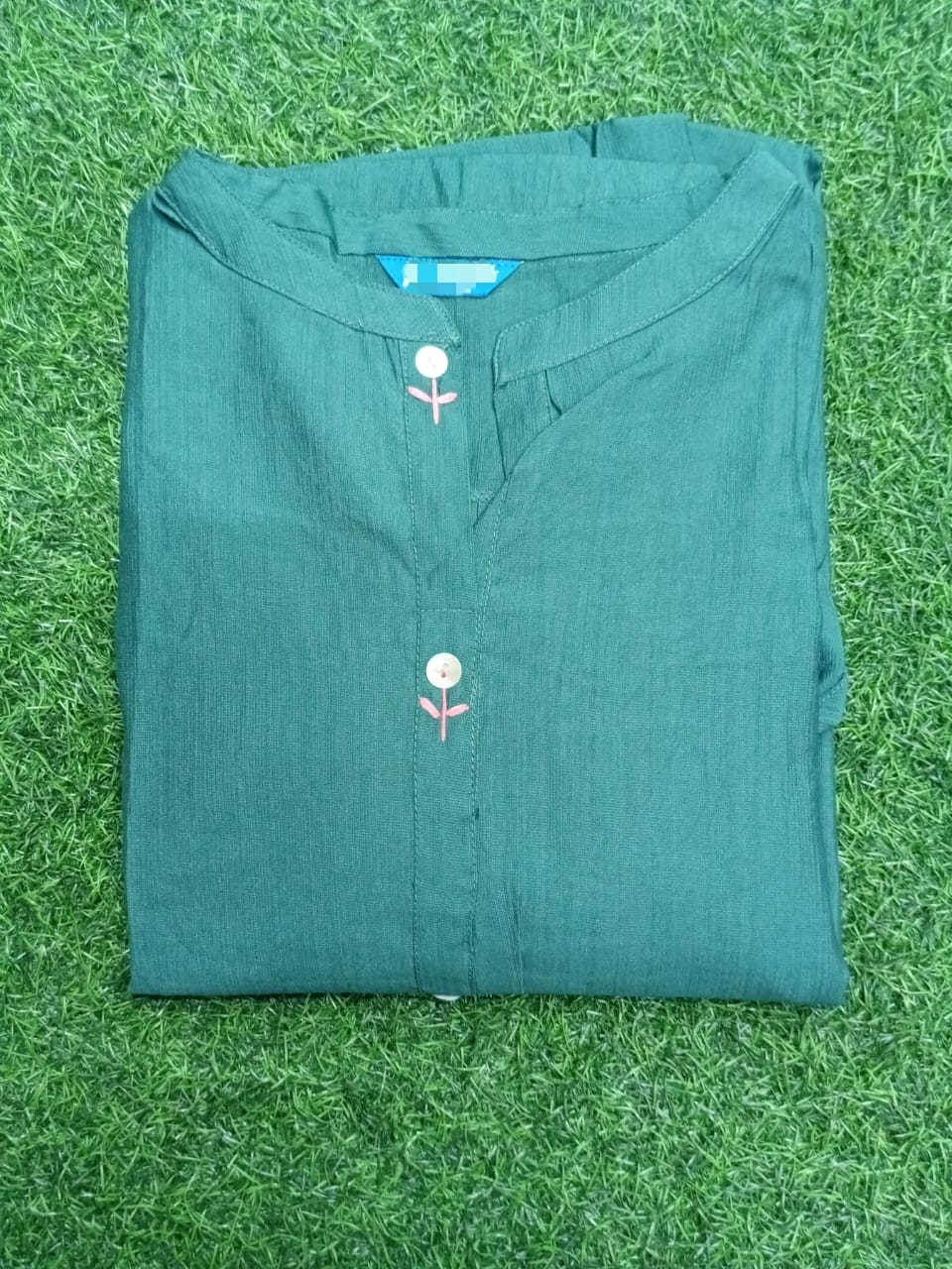 Folded teal shirt with floral designs on a grassy background