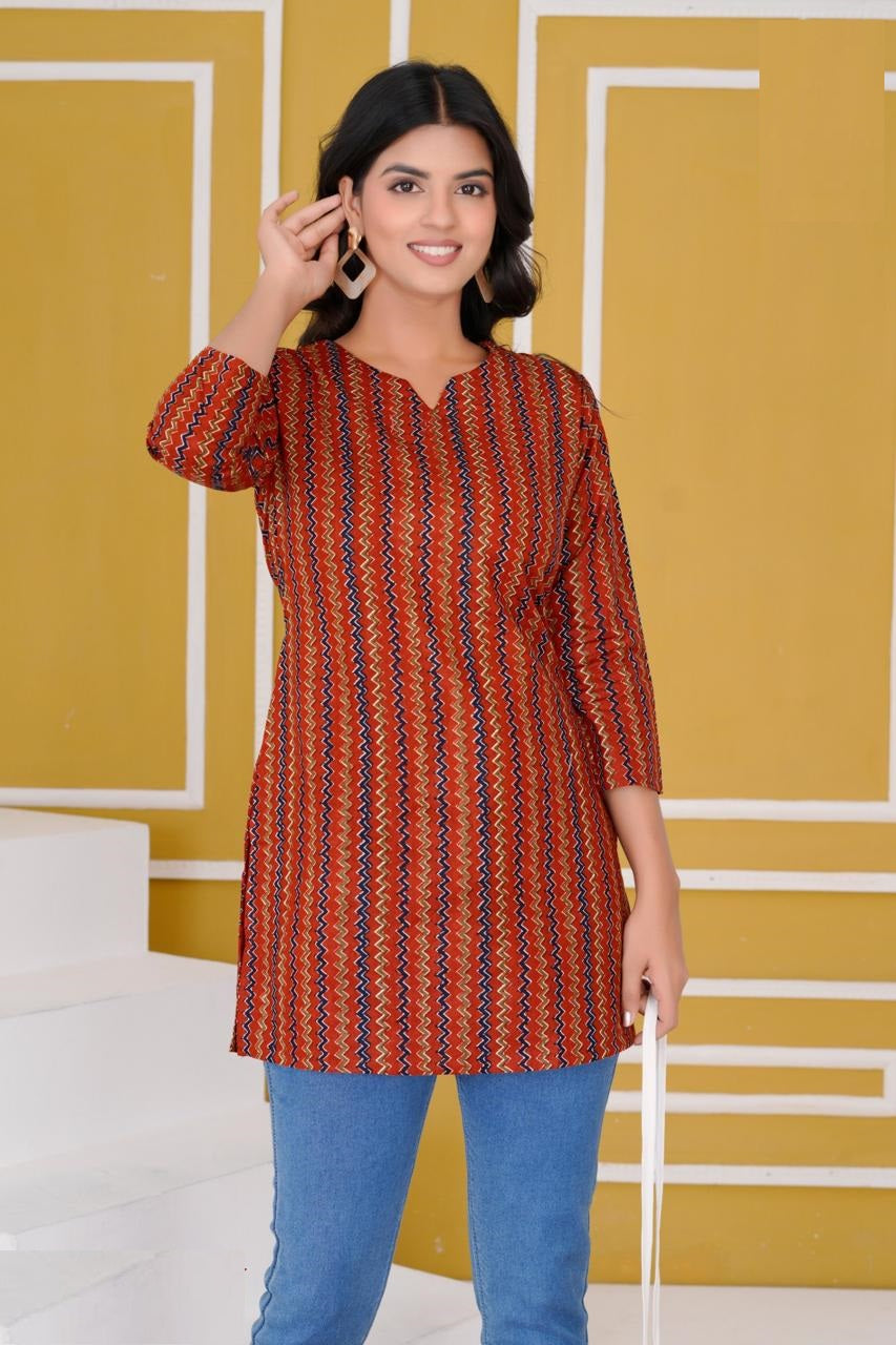 Woman wearing a patterned red and orange kurta with blue pants against a yellow wall.