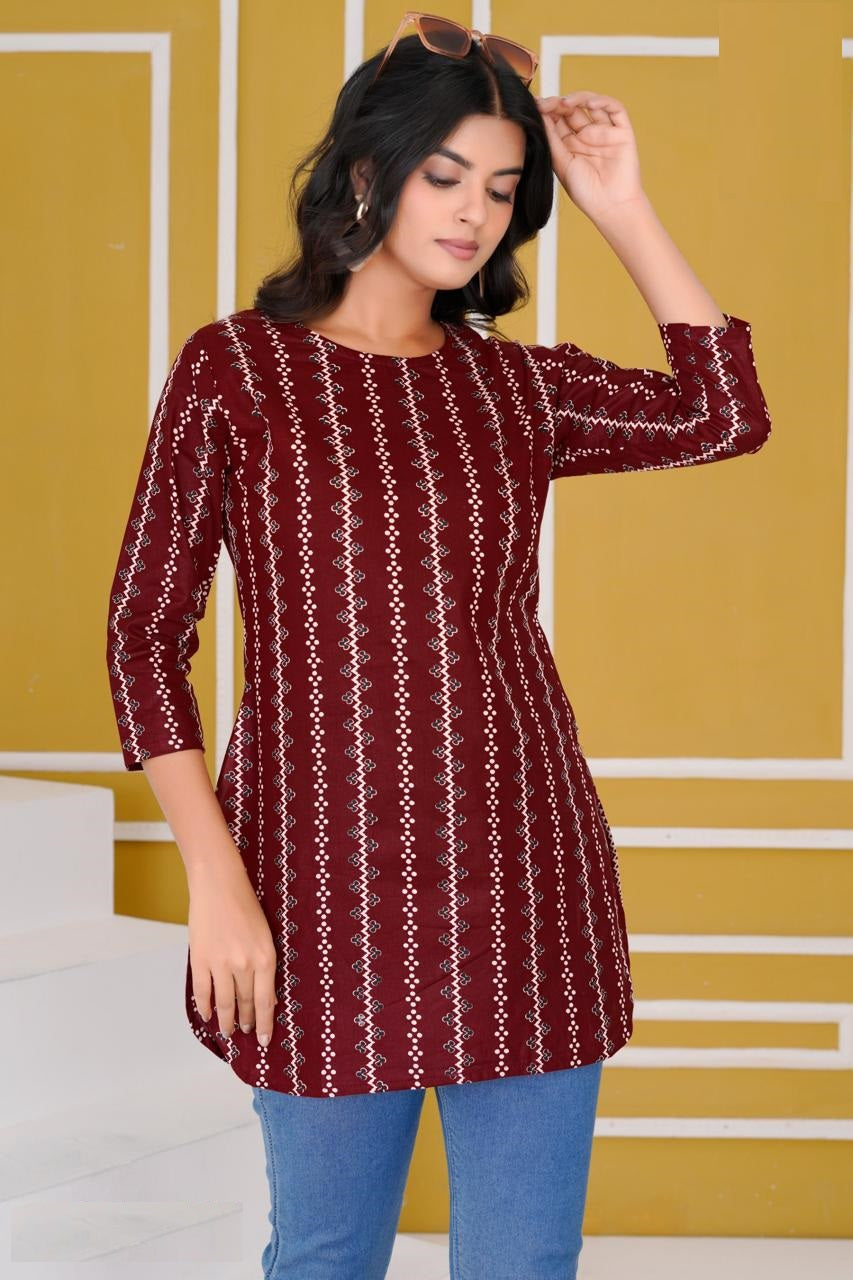 Woman wearing a maroon and white patterned dress with blue jeans against a yellow wall.