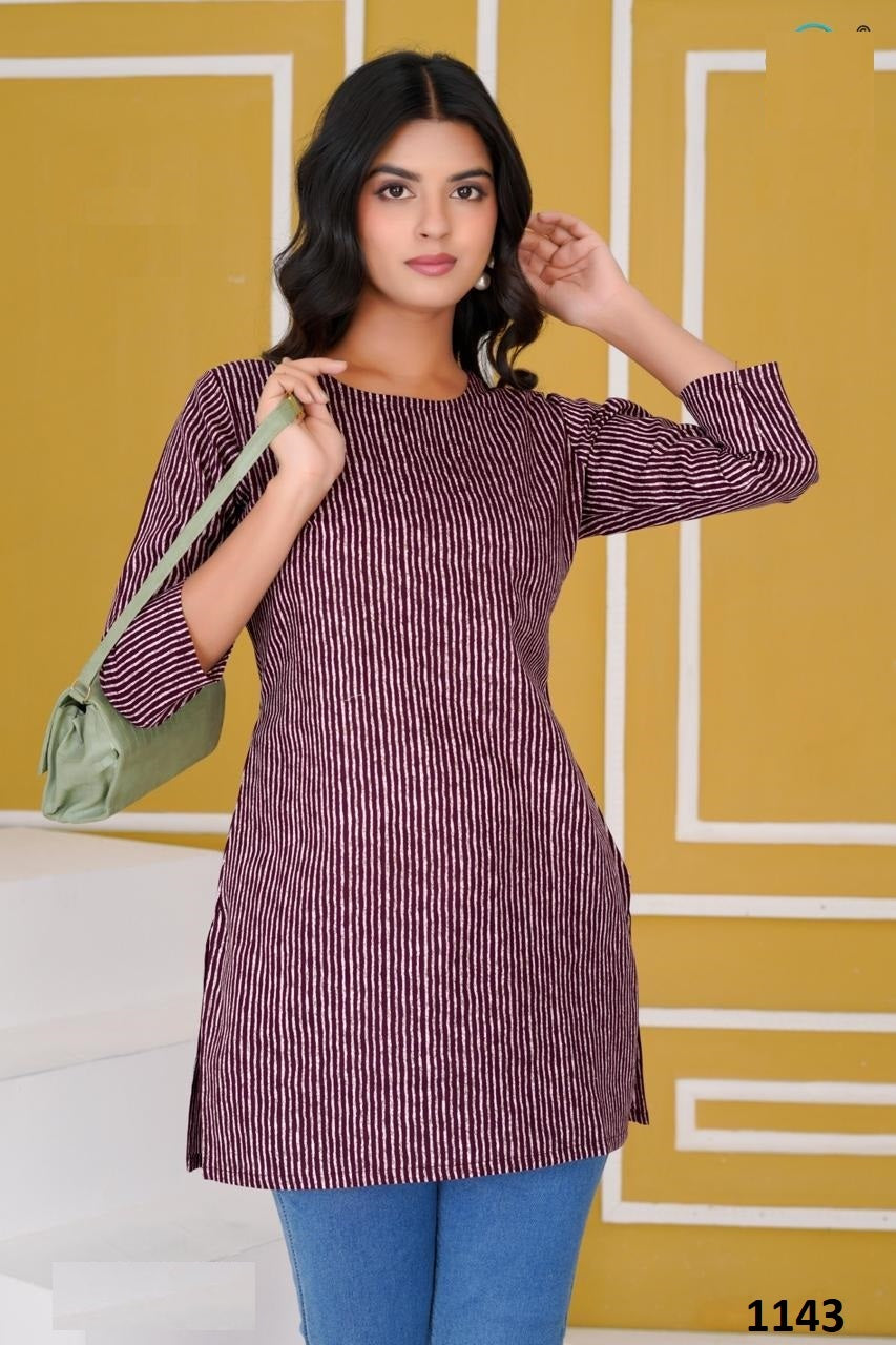 Woman wearing a striped dress with a green bag against a yellow and white geometric patterned wall.