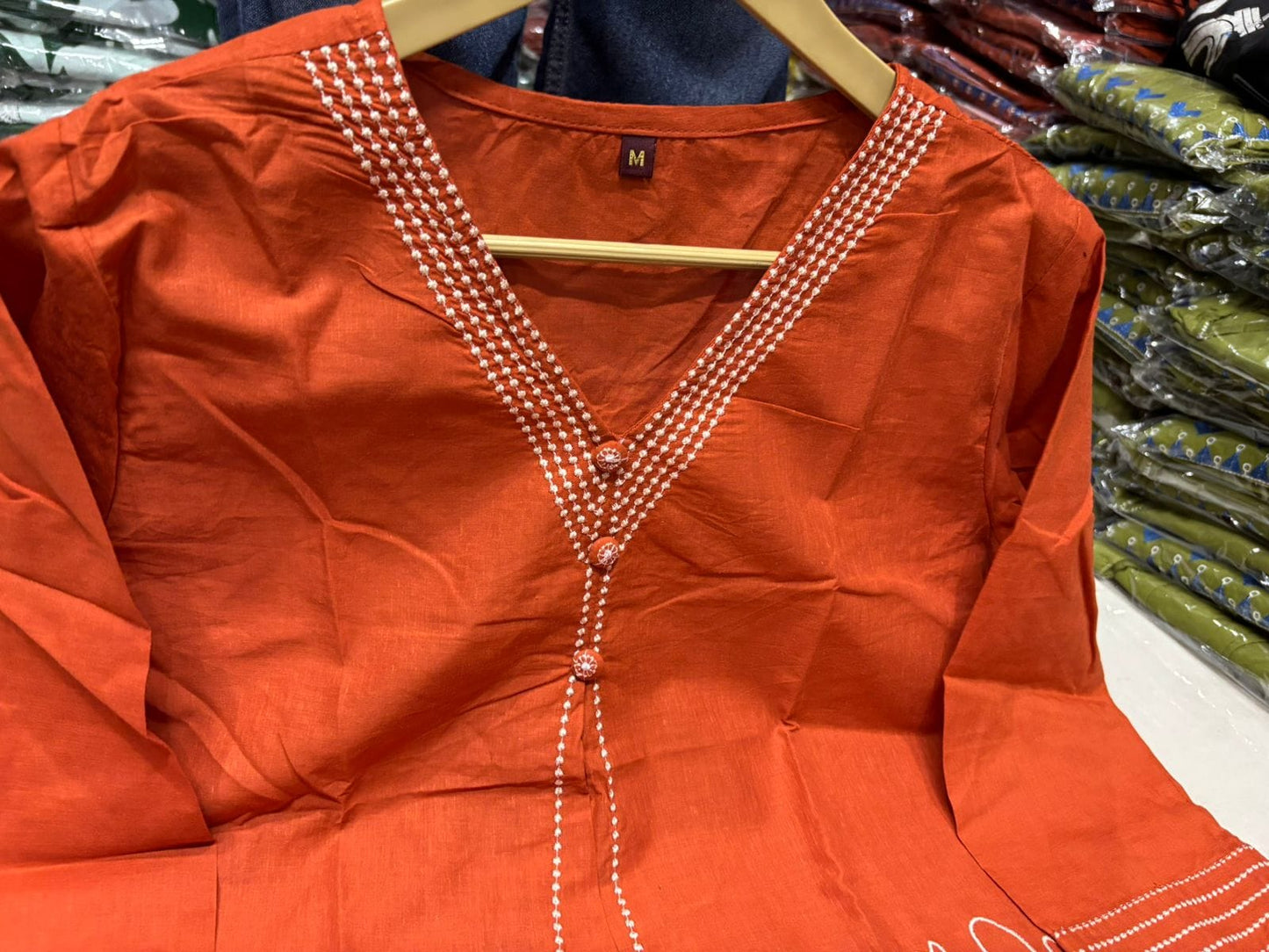 Orange blouse with pearl detailing on a hanger in a store setting