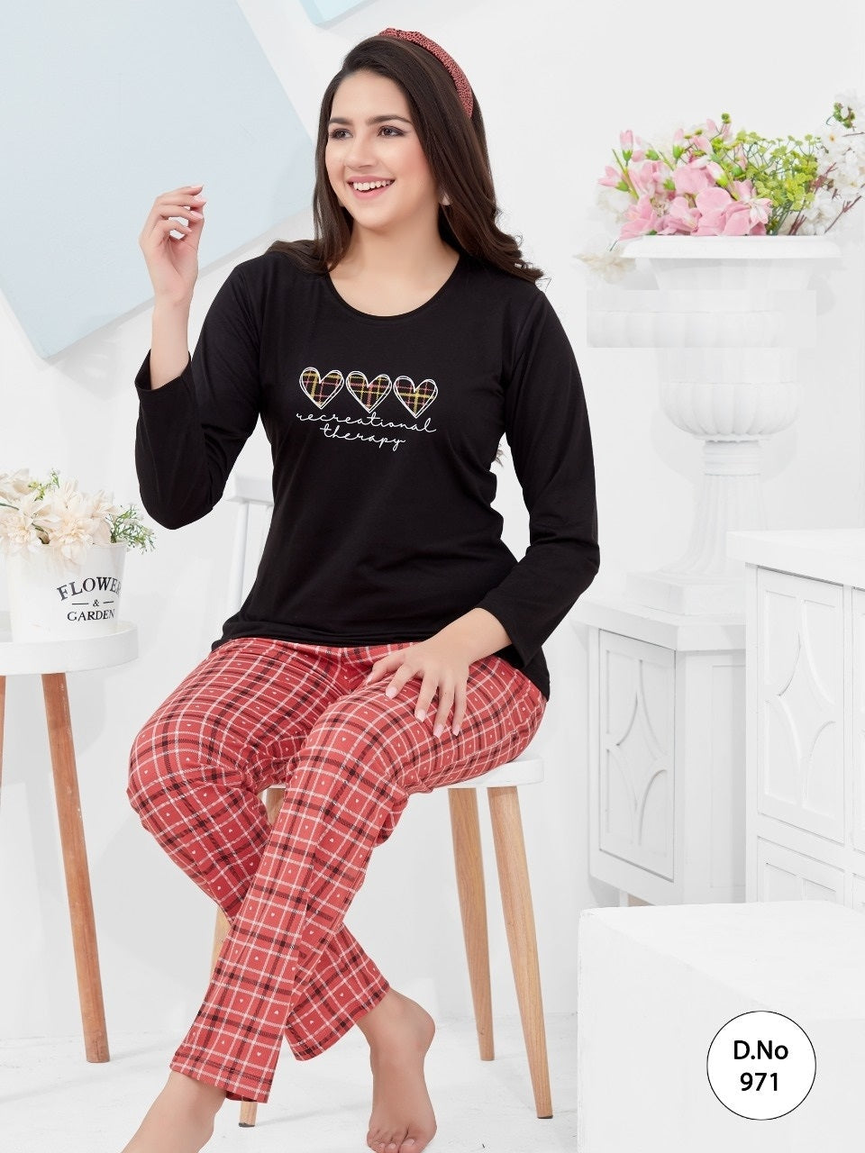A woman sitting on a chair wearing a black top with a heart and floral pattern and red checkered pants.