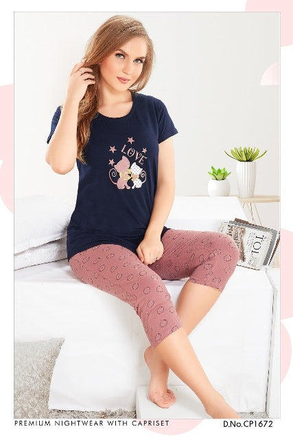 A woman sitting on a sofa wearing a navy blue and pink cat printed T-shirt with capri cotton hosiery.