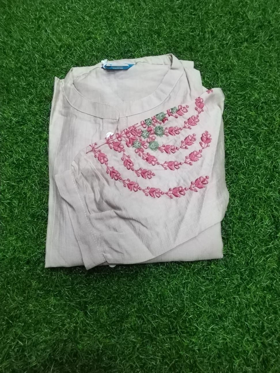 Folded light-colored shirt with pink floral embroidery on a green grass background