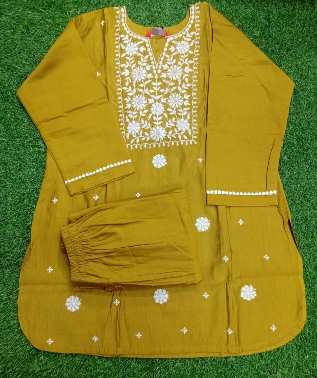Mustard yellow traditional outfit with white floral embroidery on a green background