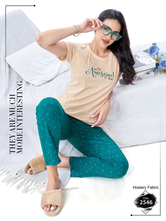 Woman wearing a beige t-shirt with 'Awesome' text and teal polka dot pants sitting on a bed.