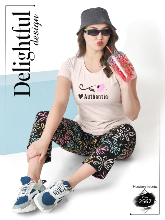 Person wearing a pink t-shirt with 'Authentic' design, colorful pants, and a gray bucket hat, sitting on a white surface.