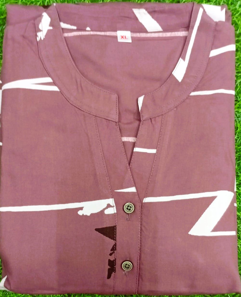 Folded mauve shirt with white stripes on a grass background