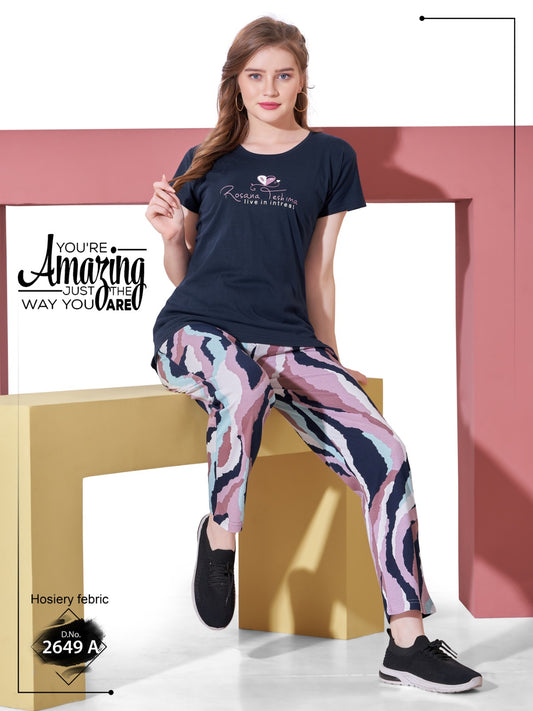 Woman wearing a navy t-shirt and patterned pants sitting on a gold bench with a white background.