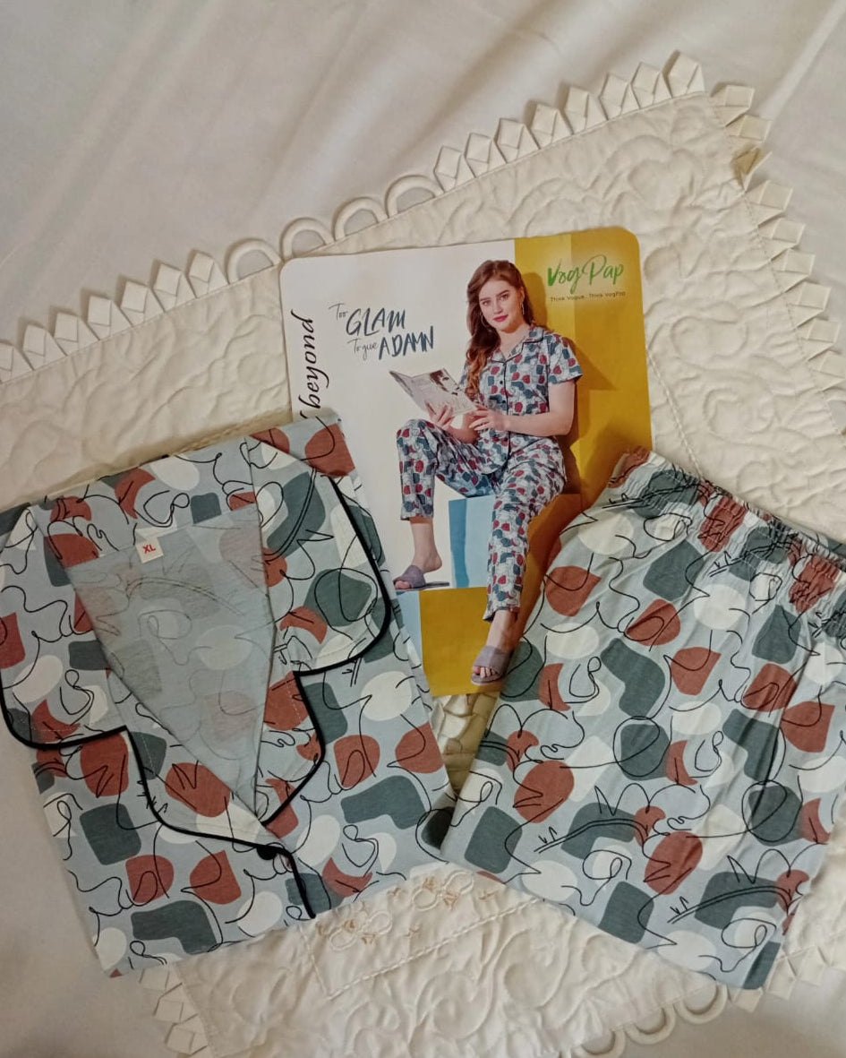 Woman in floral pajama set reading a magazine against a yellow wall.