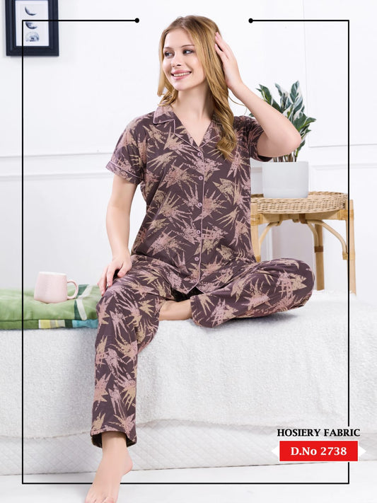 Woman wearing a patterned pajama set sitting on a couch with a plant and table in the background.