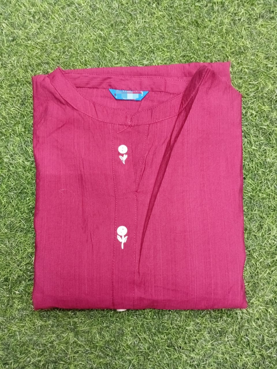 Folded maroon shirt with white floral designs on a grassy background