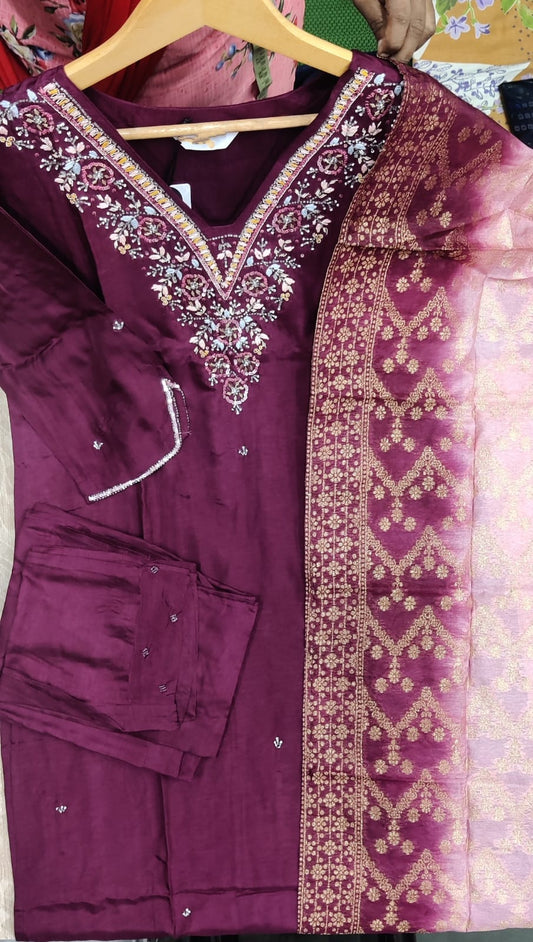 Maroon embroidered traditional outfit on a hanger with a blurred background