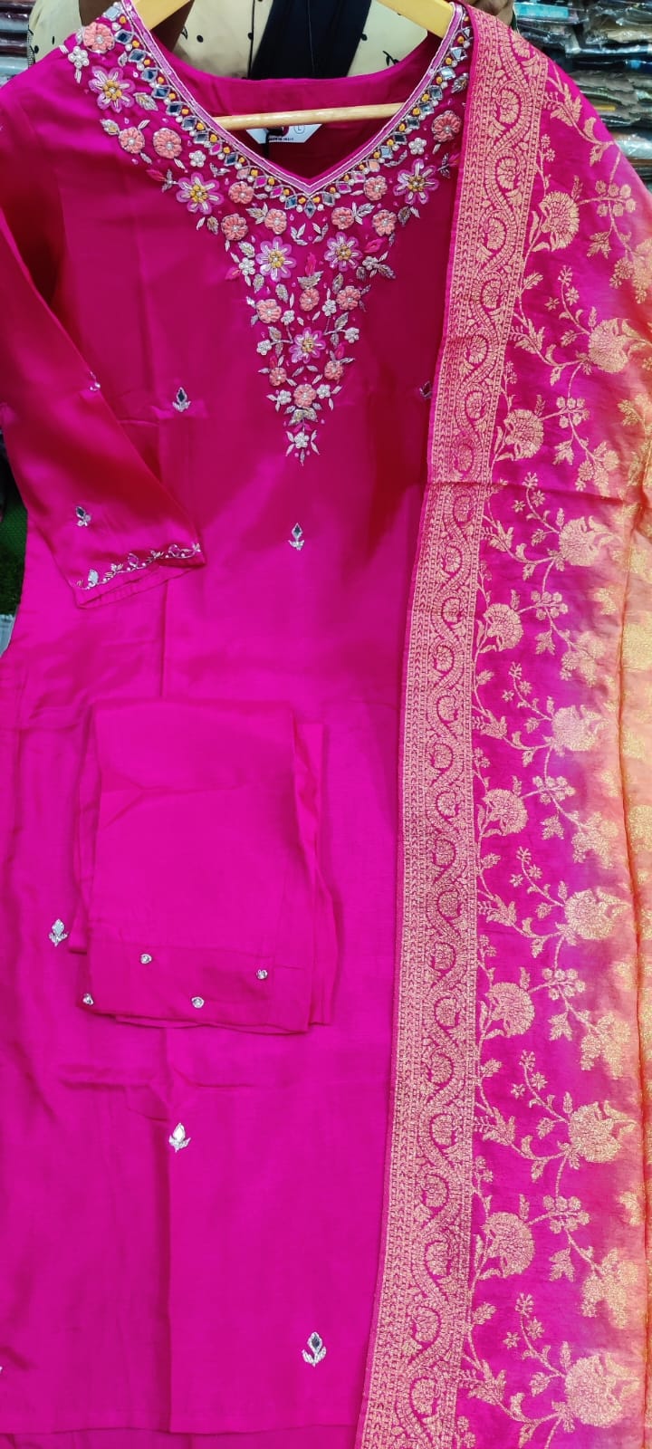 Pink traditional outfit with intricate embroidery on a hanger.