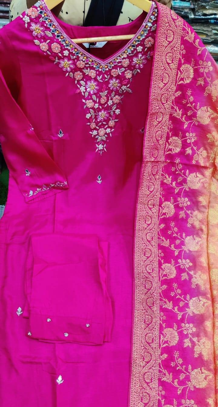 Pink traditional outfit with intricate embroidery on a hanger.