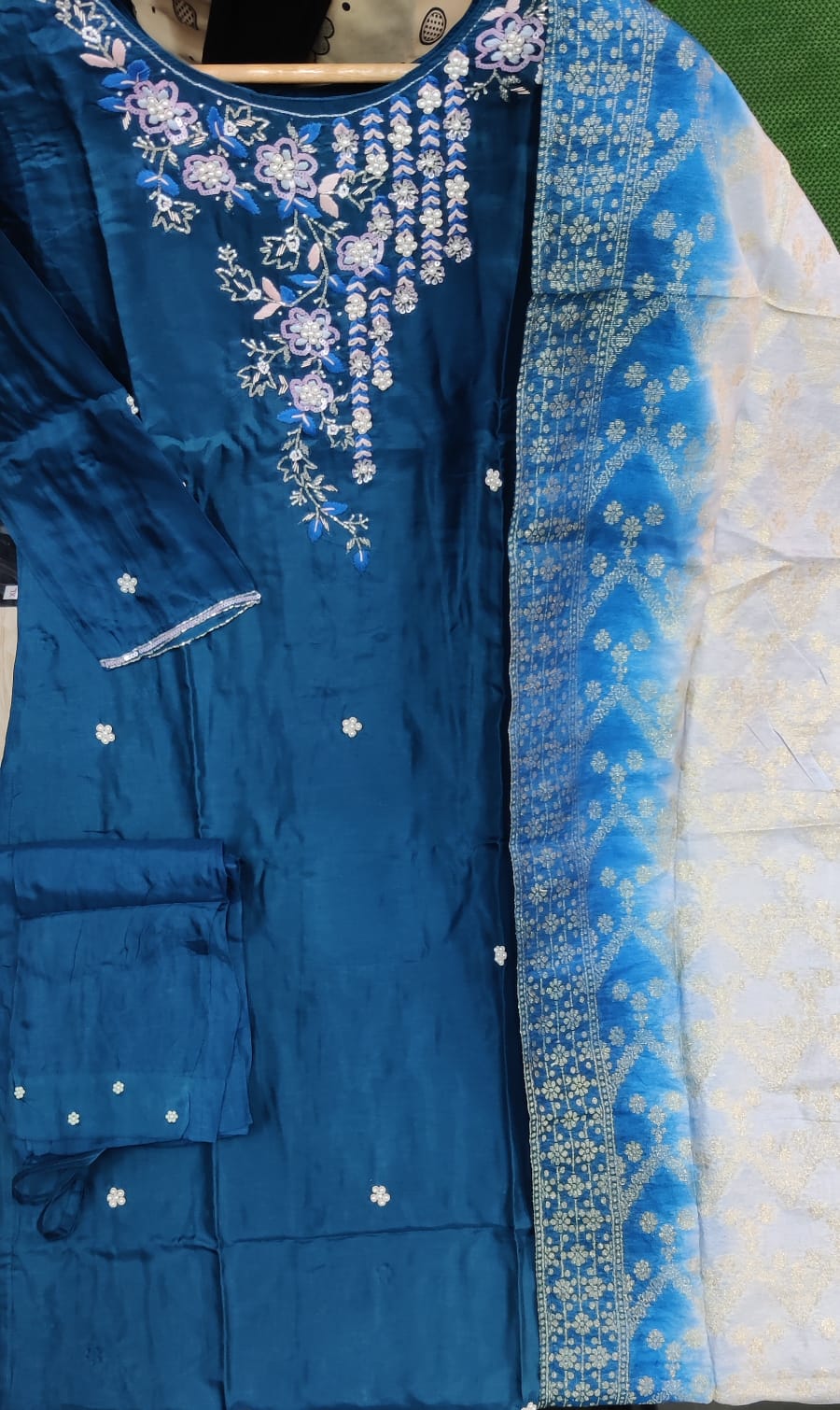 Blue embroidered traditional outfit with white floral patterns on a green background