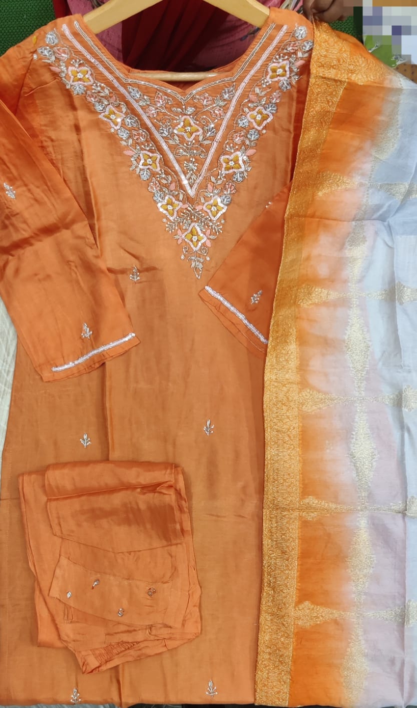 Orange traditional outfit with intricate white embroidery on a plain background