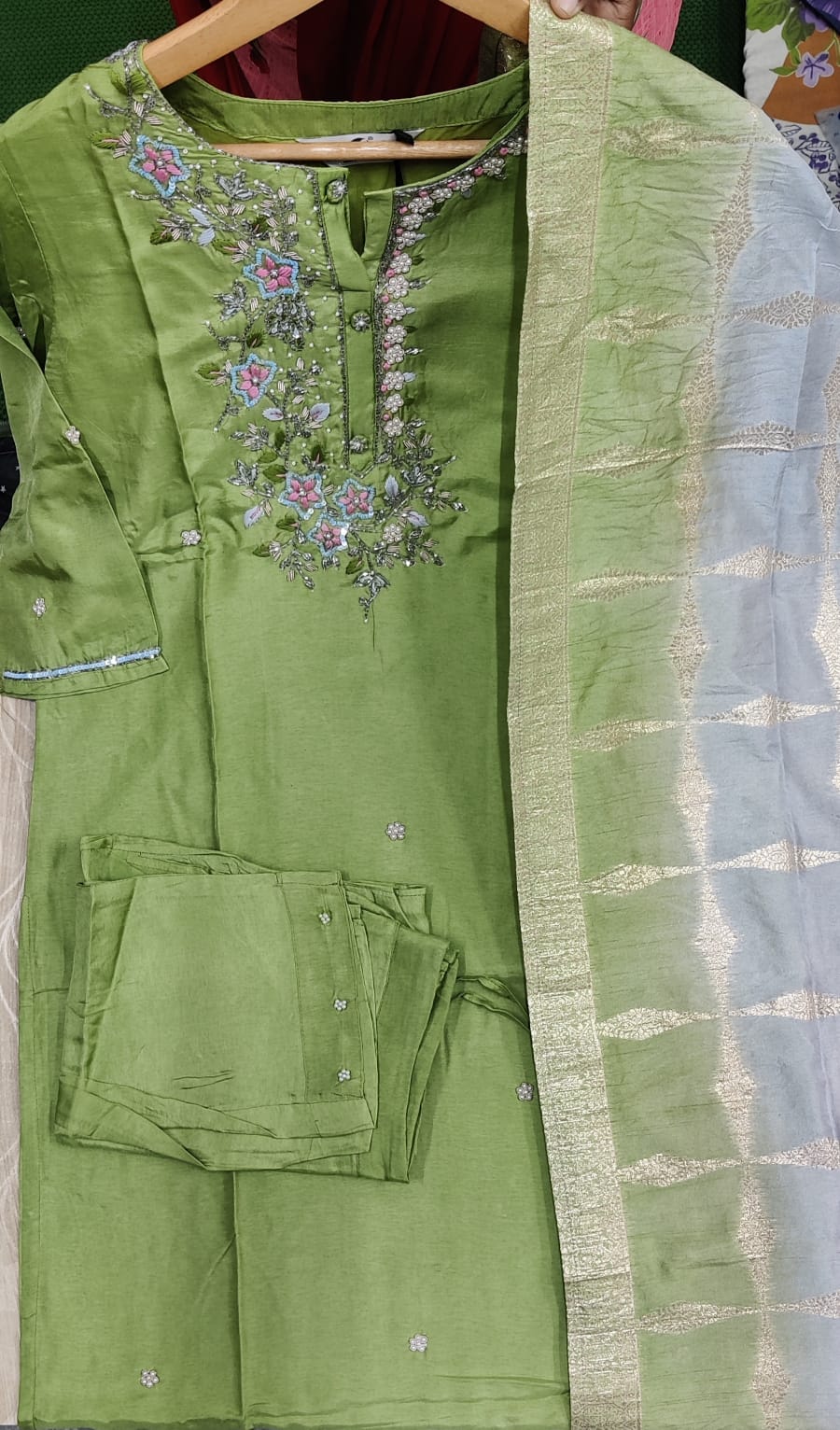 Green embroidered traditional outfit with a plain green dupatta on a hanger.