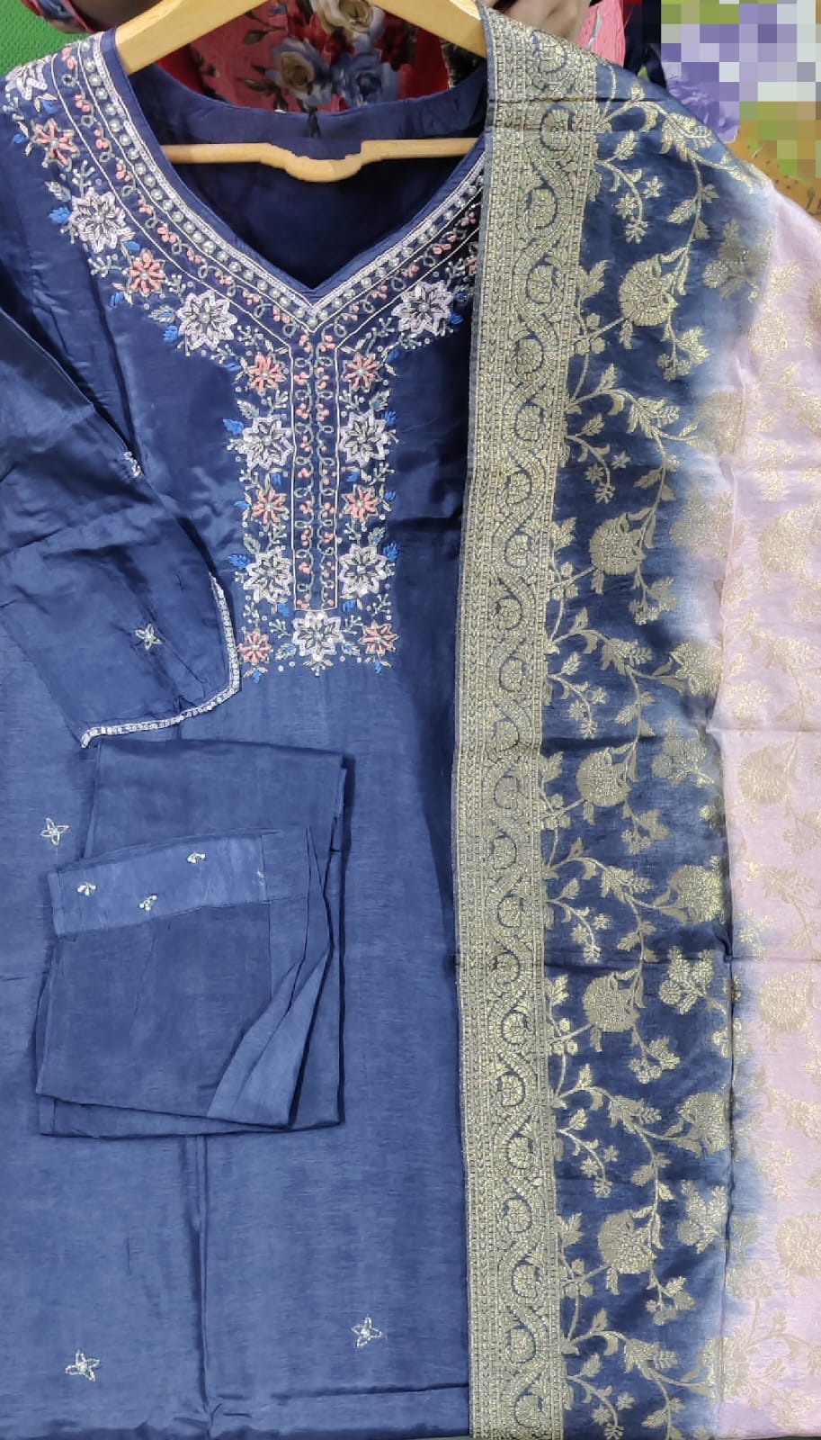Blue embroidered traditional outfit with a green border on a hanger