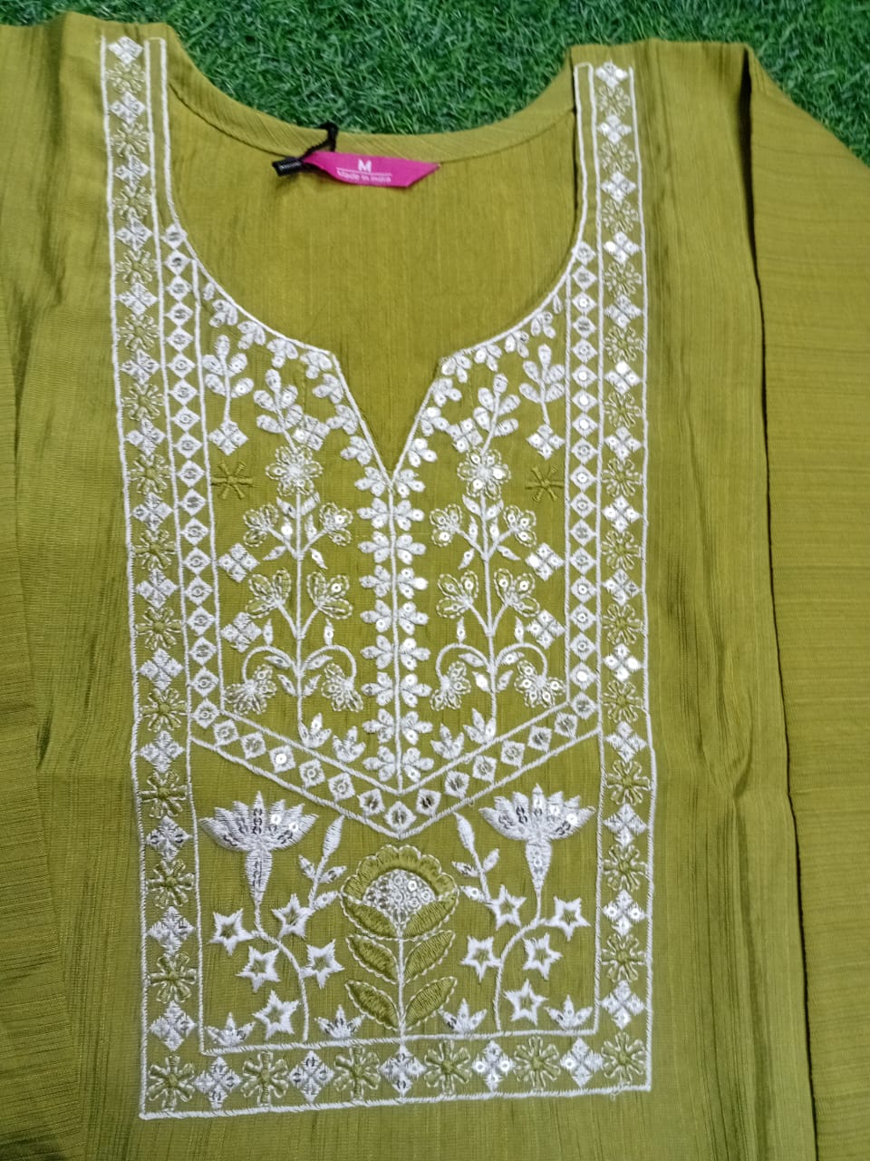 Green embroidered garment on a grassy background