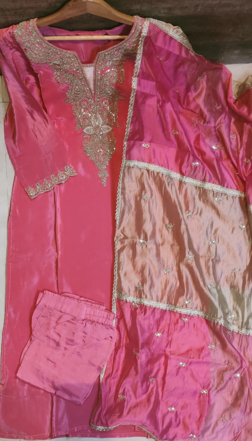 Pink traditional outfit with intricate embroidery on a wooden surface