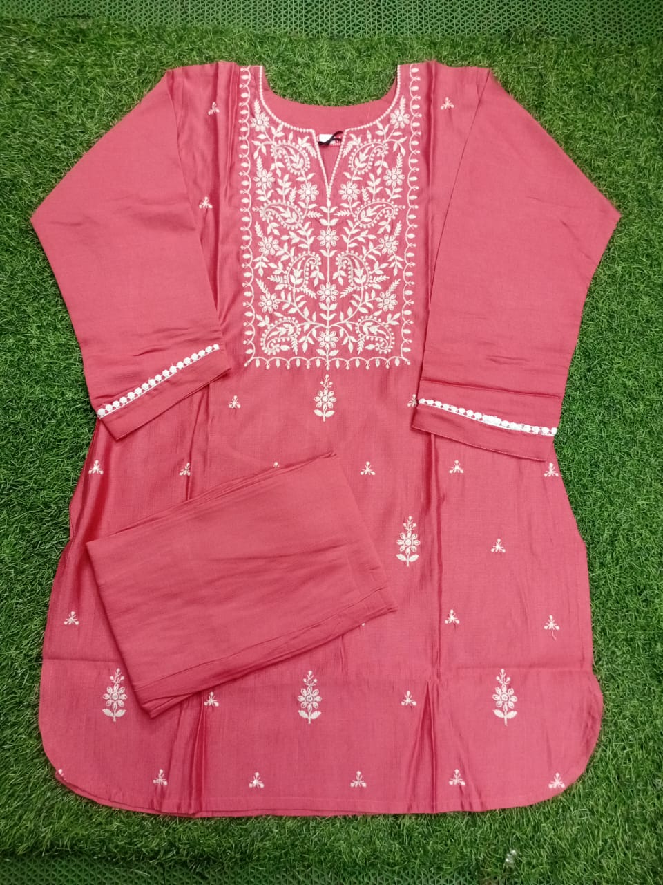 Pink traditional outfit with white embroidery on a green grass background