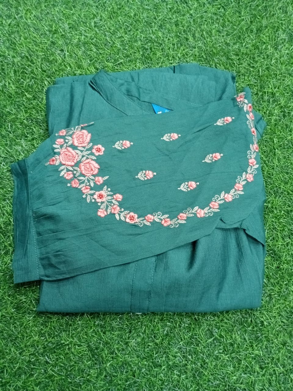 Green blouse with floral embroidery on a green grass background