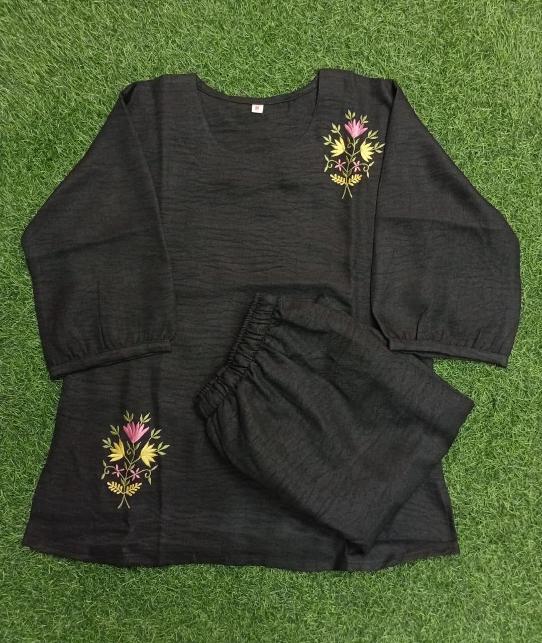 Black outfit with floral embroidery on a green grass background
