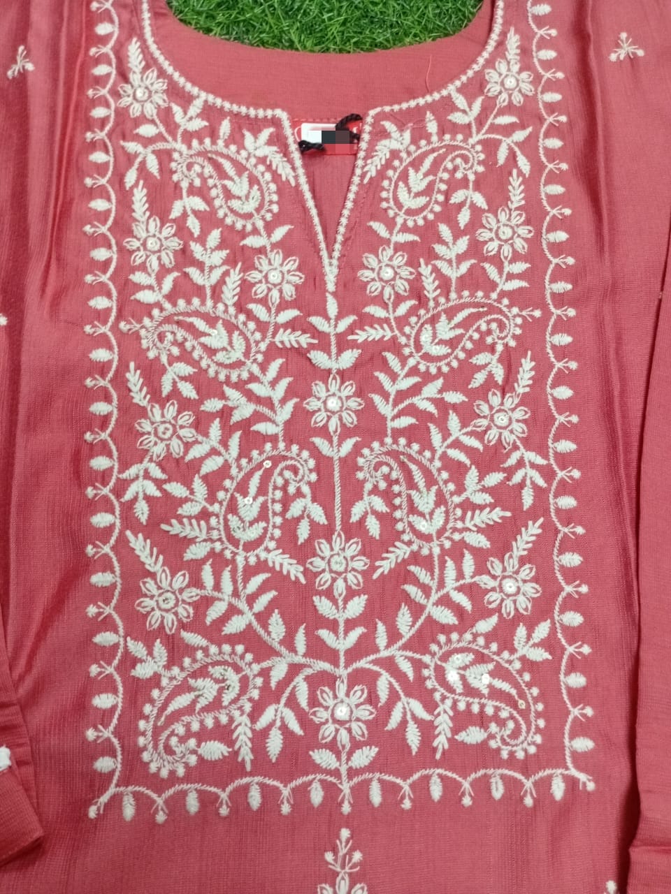 Pink embroidered garment with white floral patterns on a green grass background