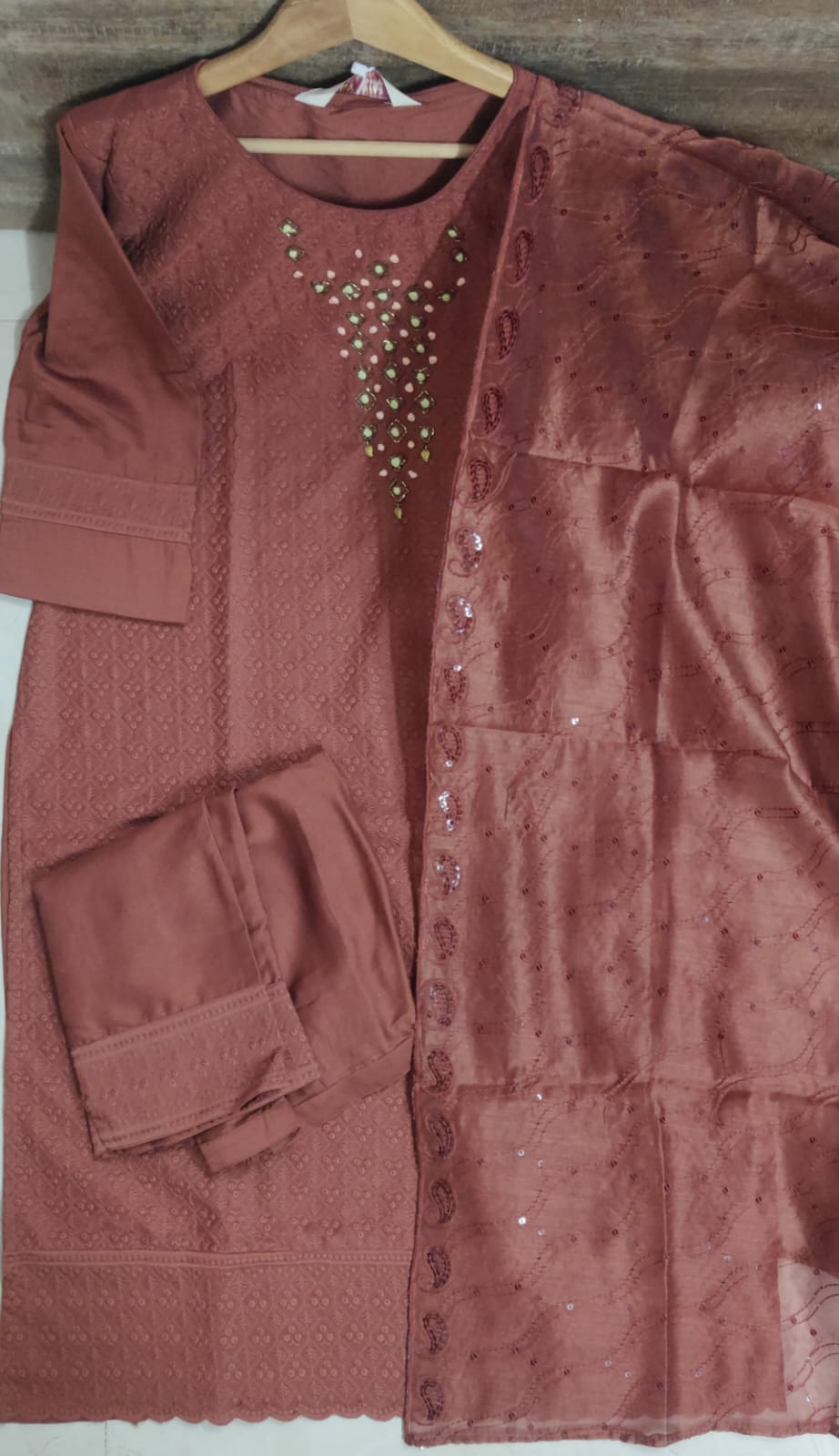 Brown textured garment with embellishments on a hanger against a wooden background