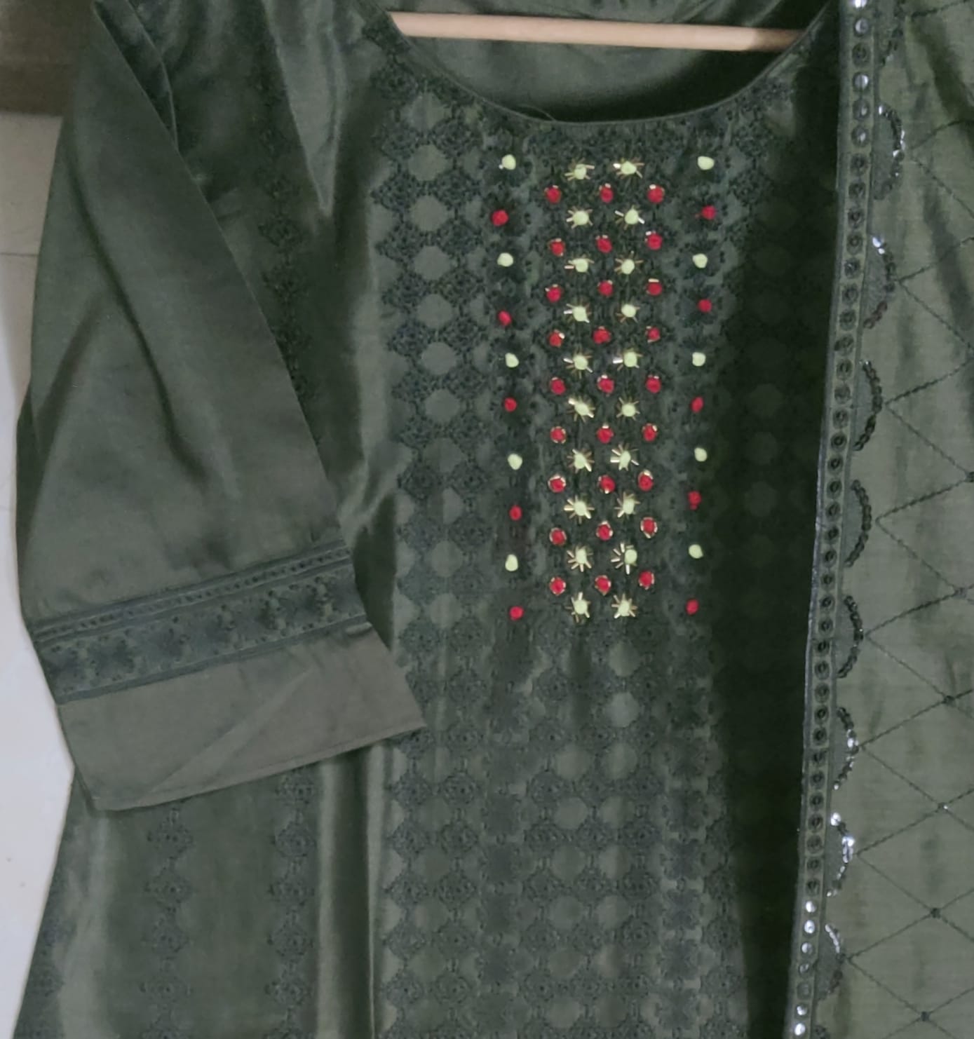 Green embroidered traditional outfit with red and gold details on a plain background