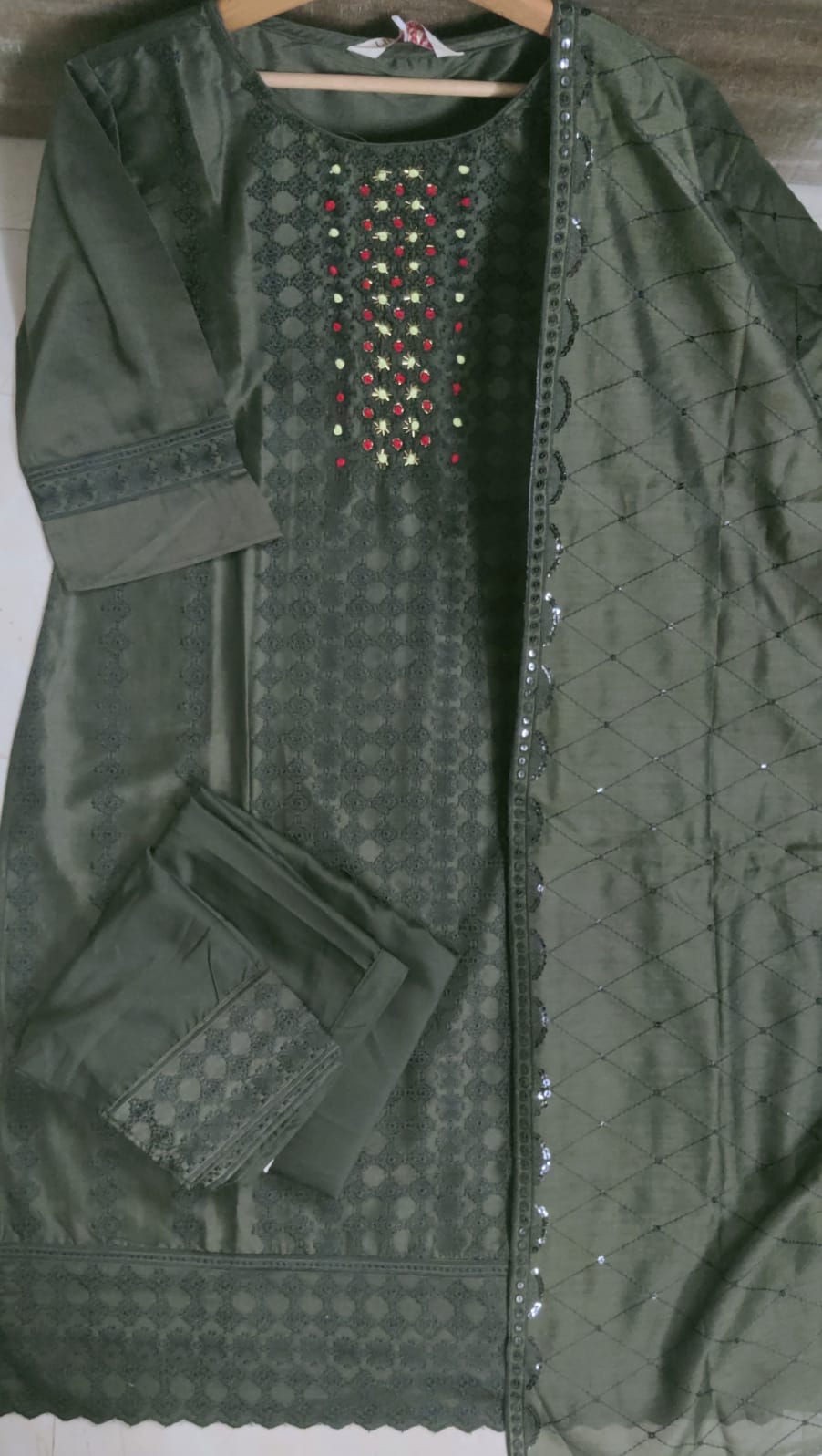 Green embroidered garment on a hanger with a plain background