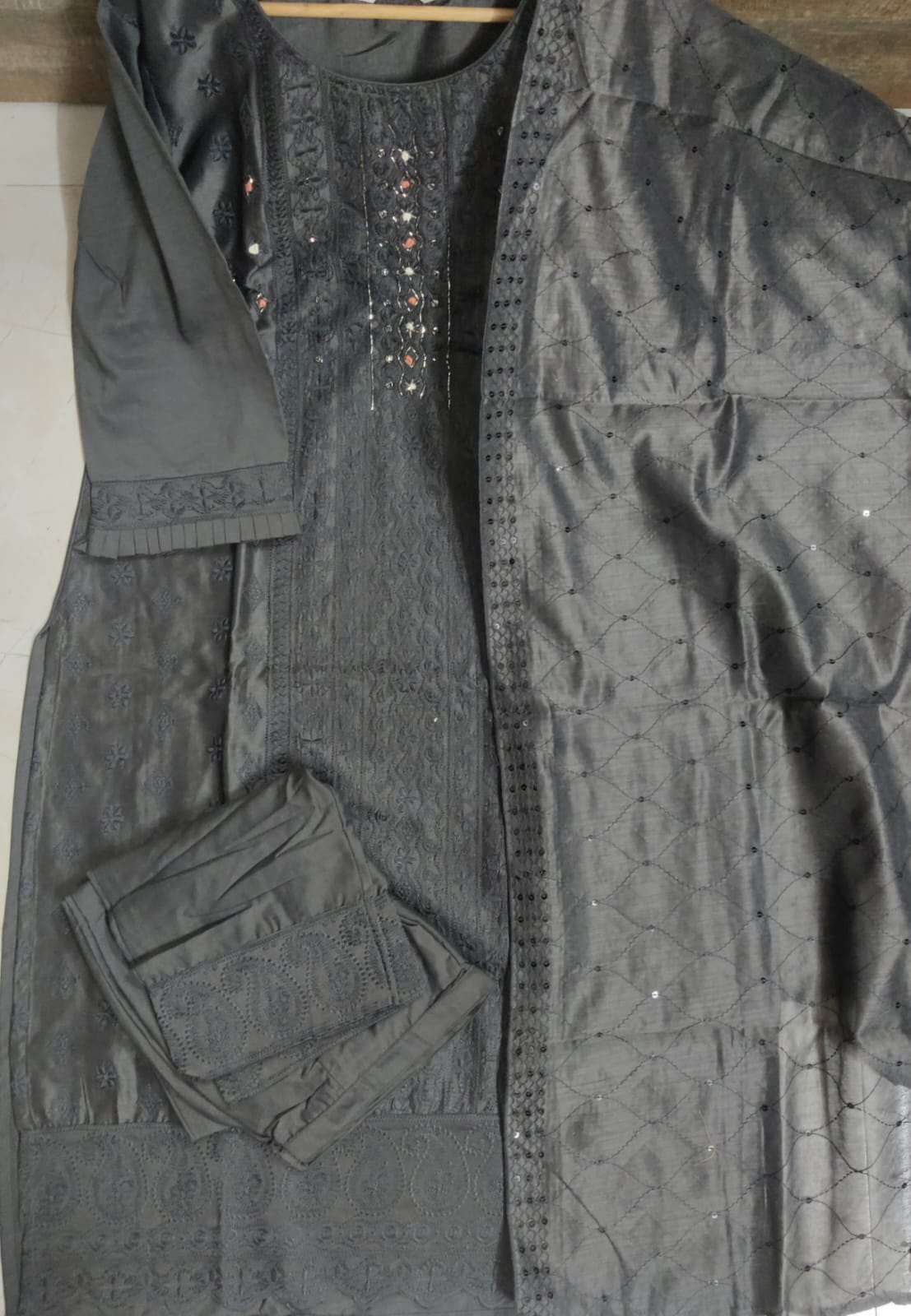 Dark gray jacket with intricate patterns and embellishments on a wooden surface