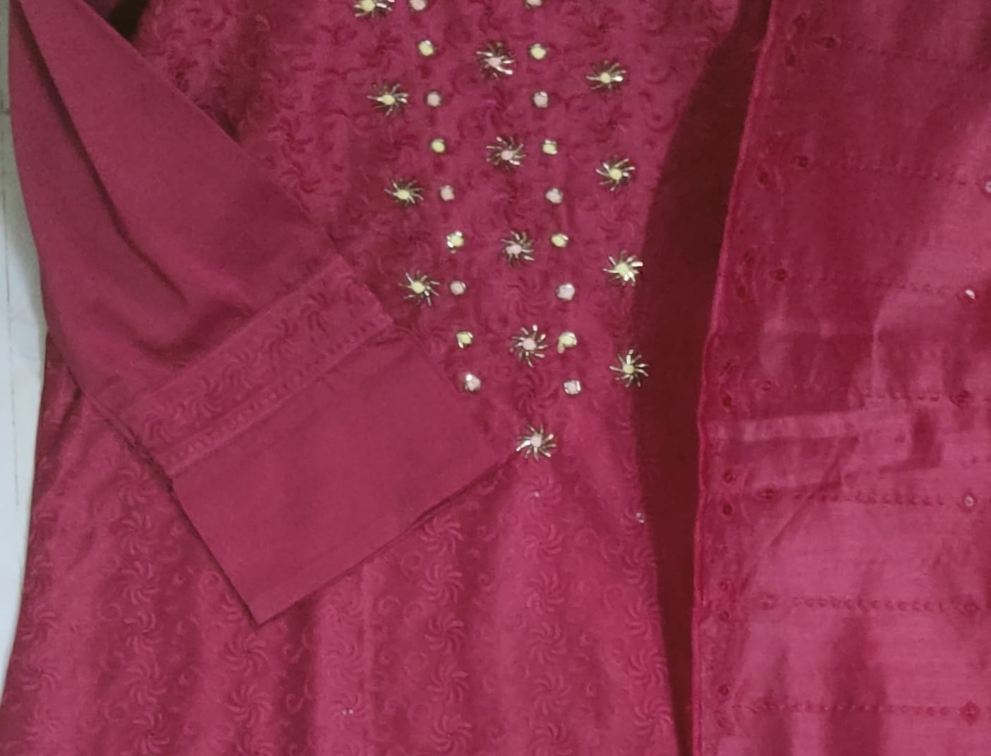 Close-up of a red garment with gold embellishments on a white background