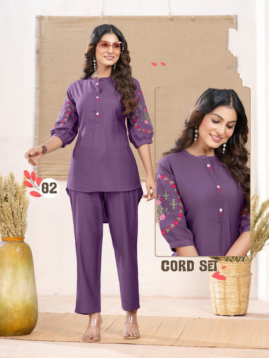 Two women wearing purple outfits with floral embroidery on a neutral background