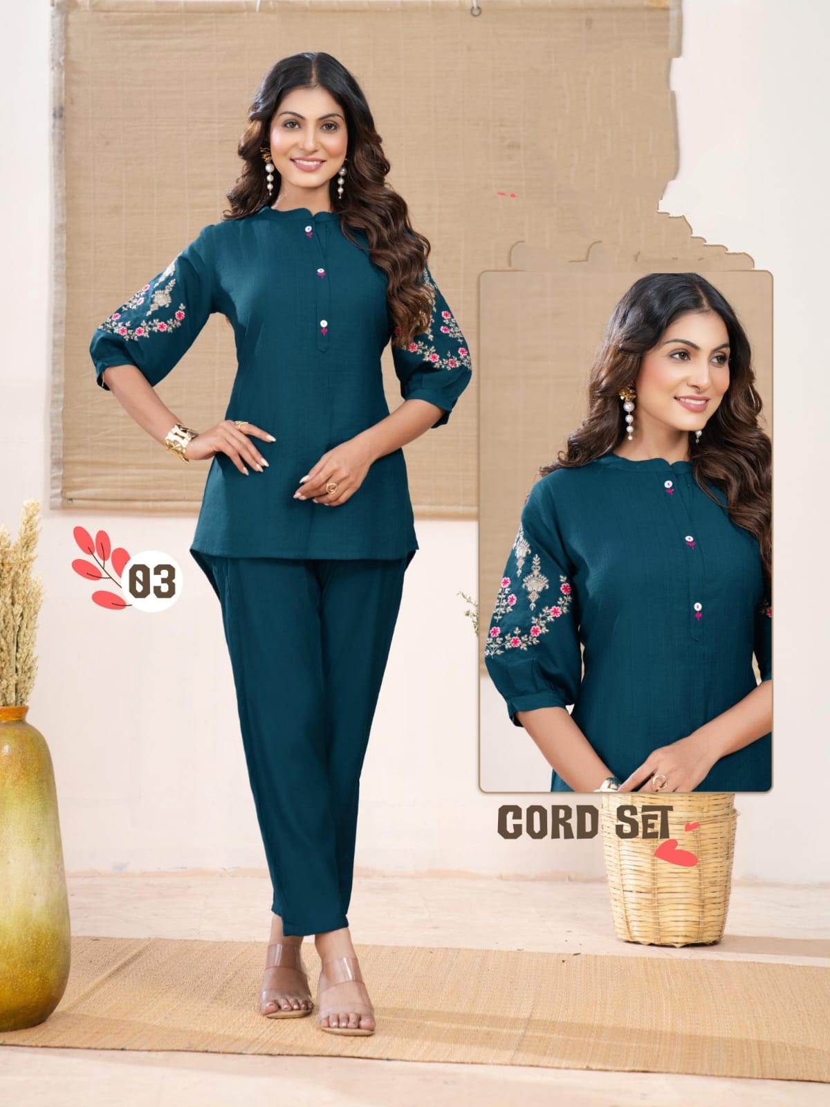 Woman wearing a teal outfit with floral embroidery, standing in a minimalistic setting.