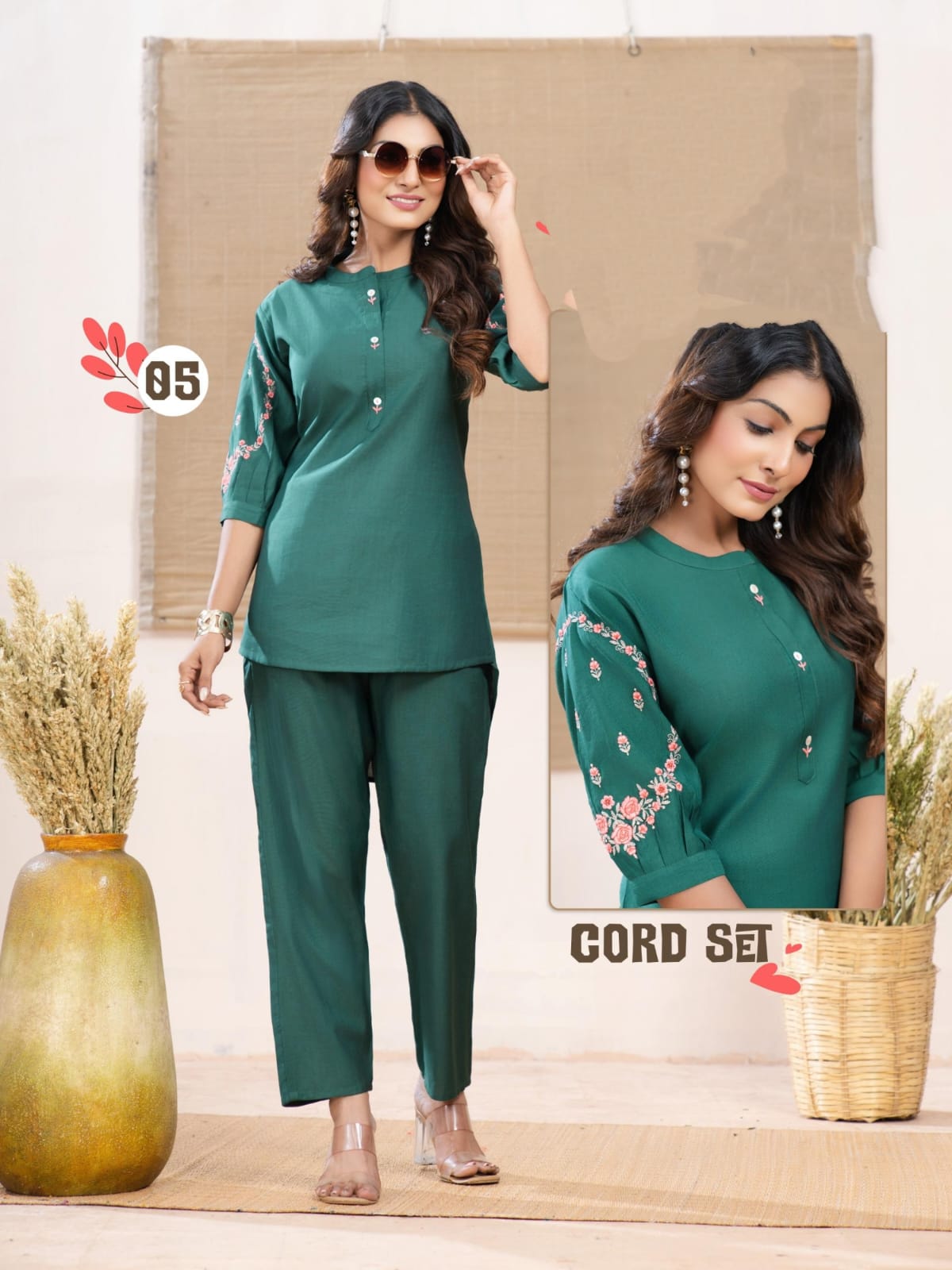 Woman wearing a green outfit with floral embroidery, standing in front of a neutral background.