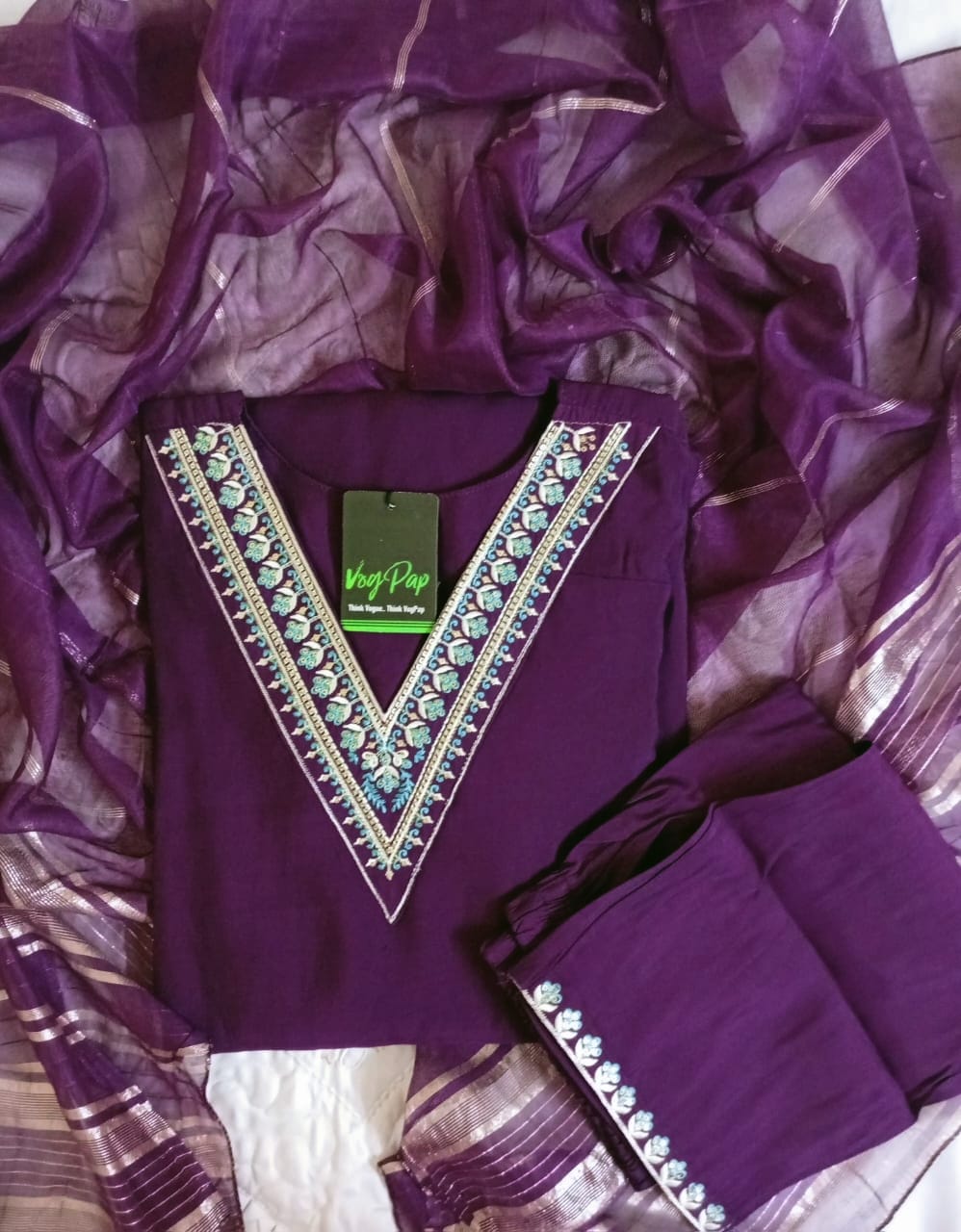 Purple embroidered garment with a green tag on a textured fabric background
