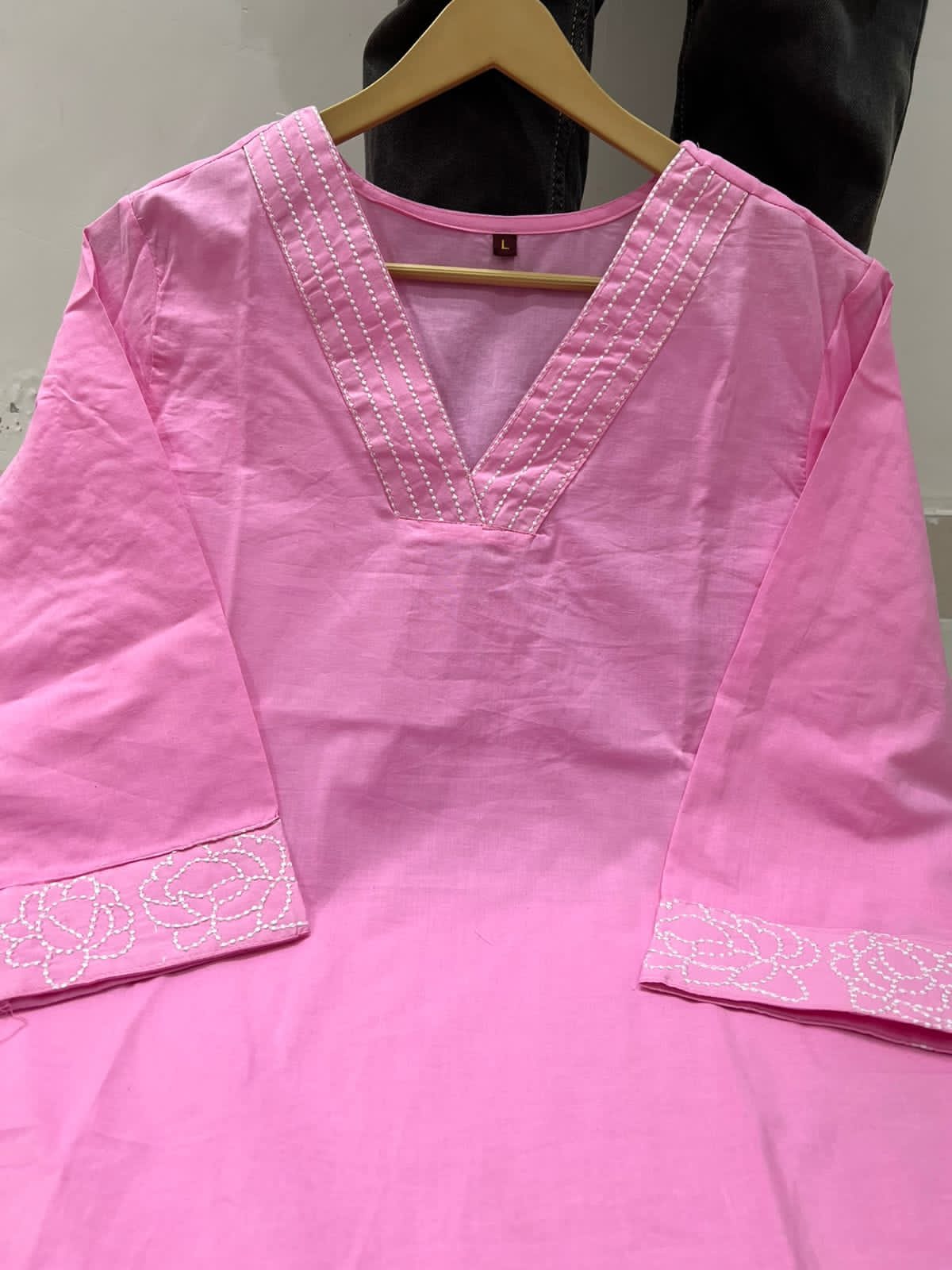 Pink traditional outfit with white embroidery on a hanger against a neutral background