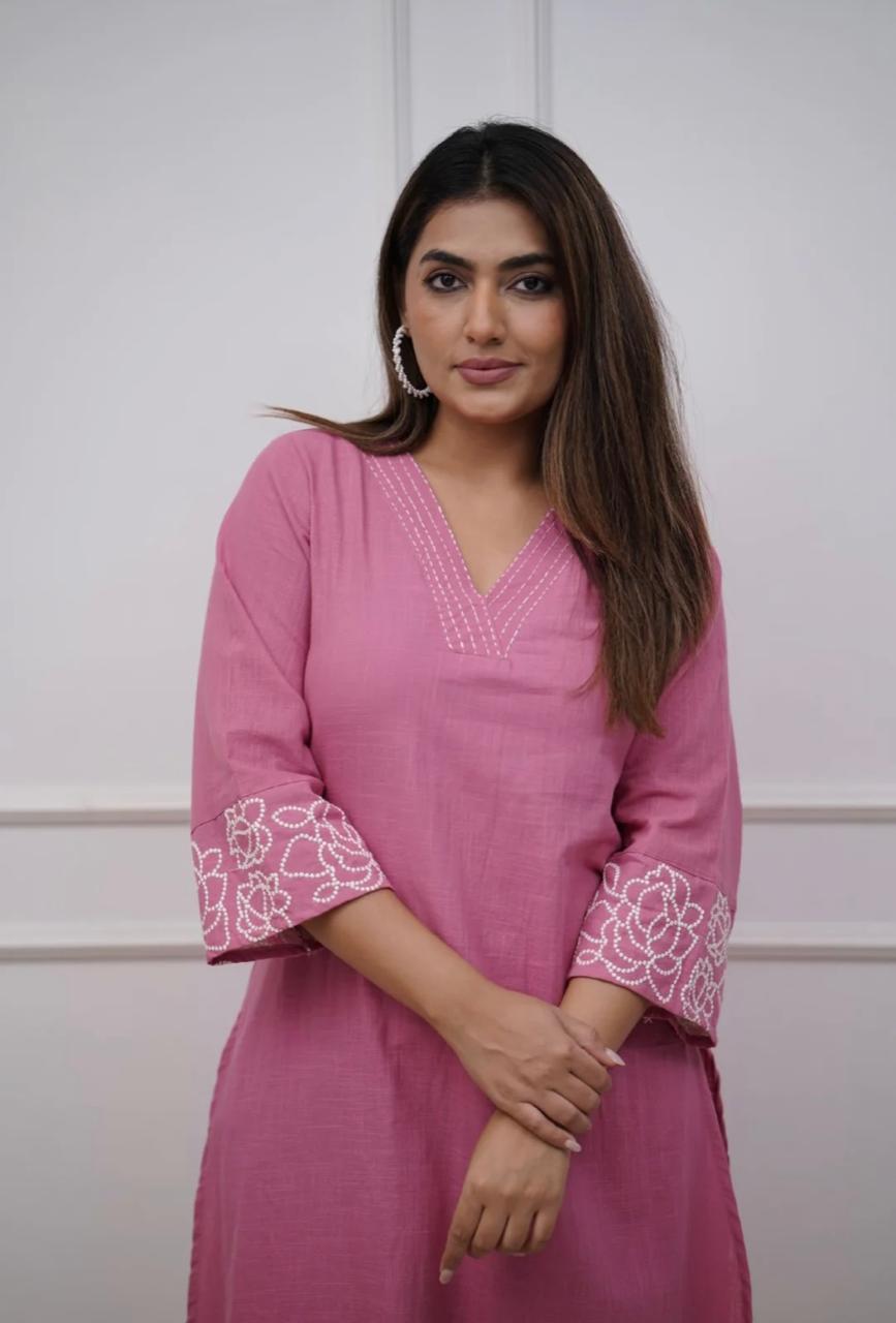 Woman wearing a pink dress with white embroidery against a plain background