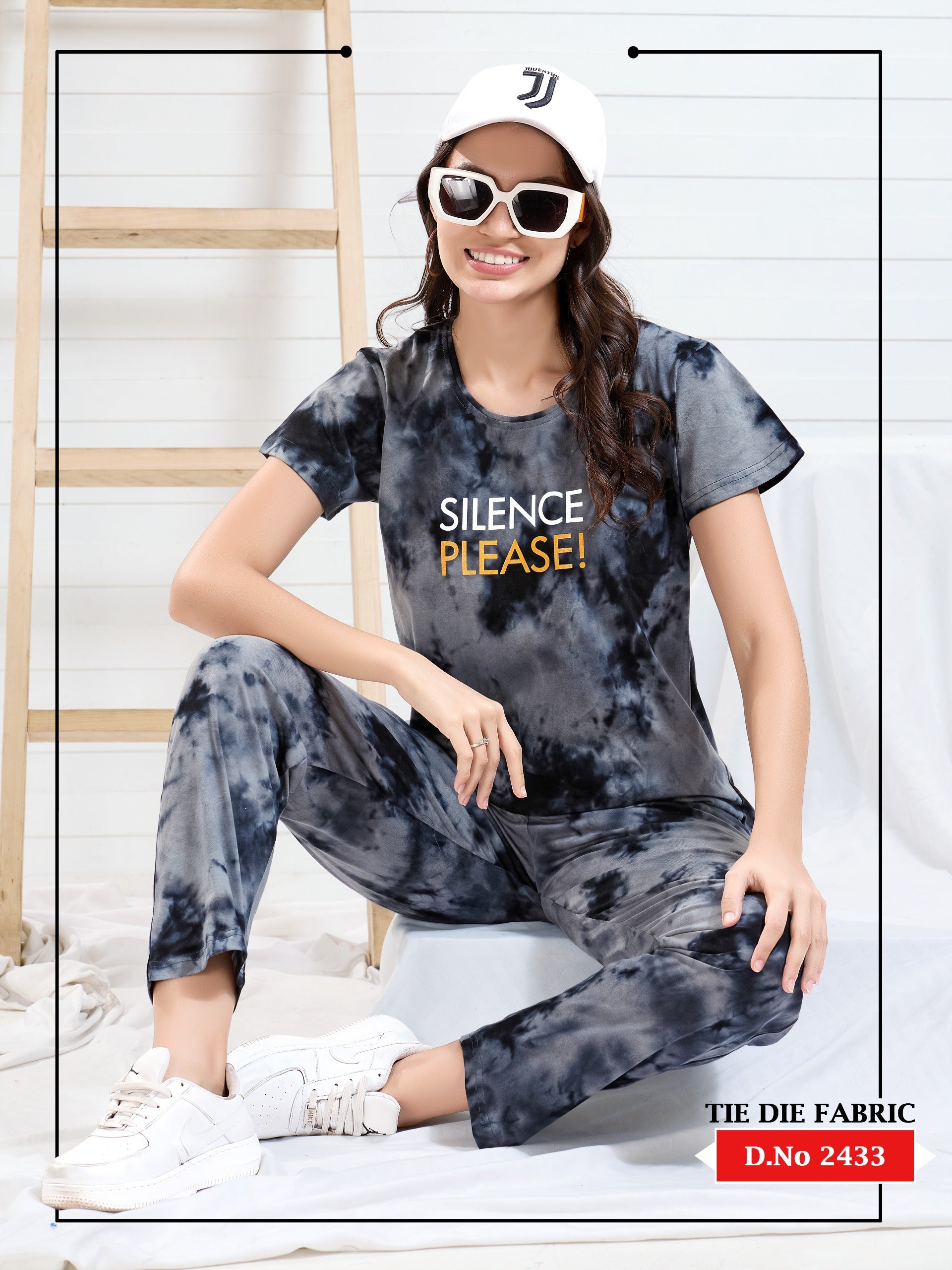 Person wearing a tie-dye outfit with 'Silence Please!' text, sitting on a stool.