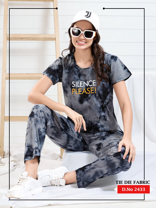 Person wearing a tie-dye outfit with 'Silence Please!' text, sitting on a stool.