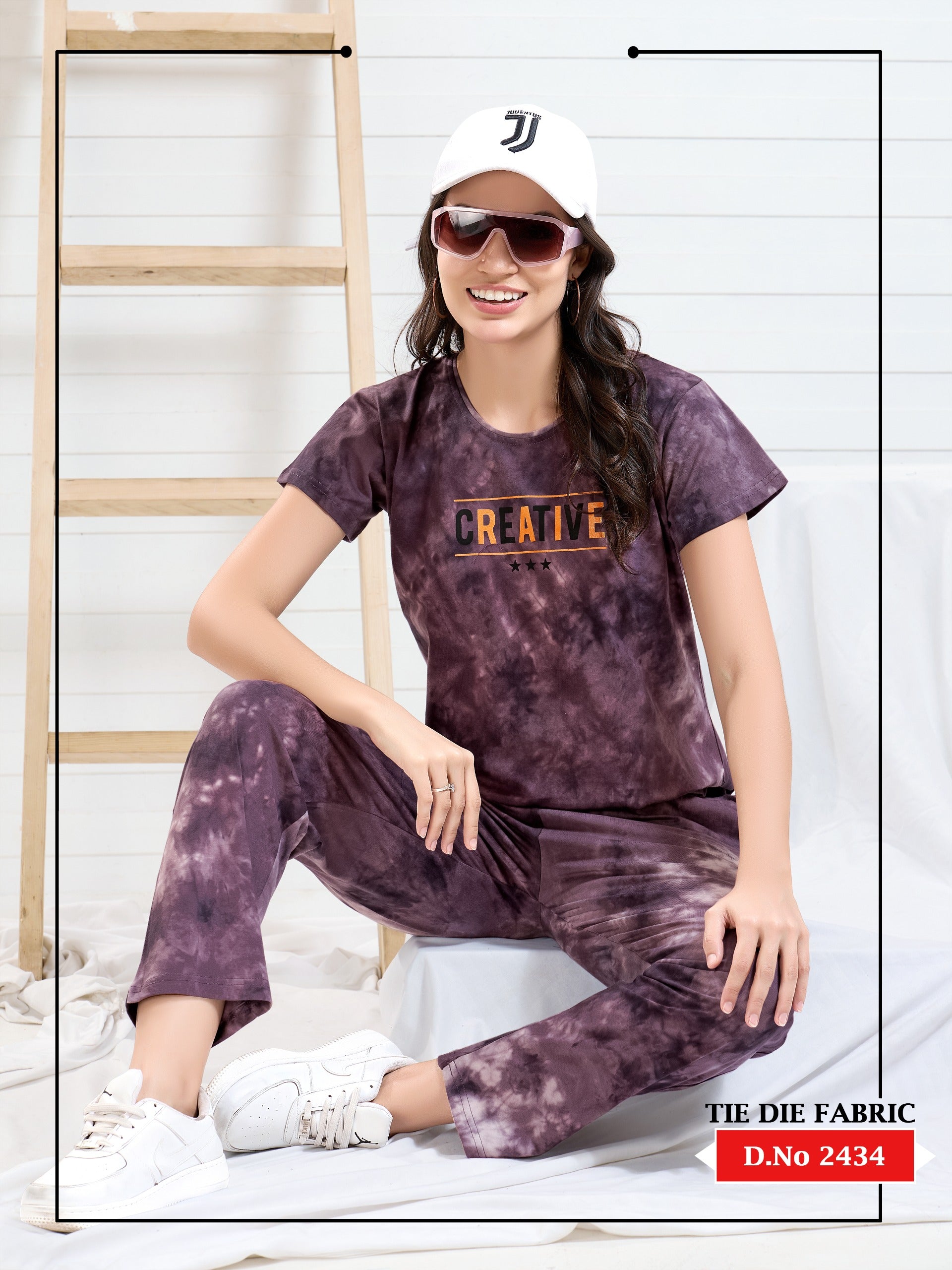 Woman wearing a tie-dye outfit with a visible brand logo, sitting against a white background.