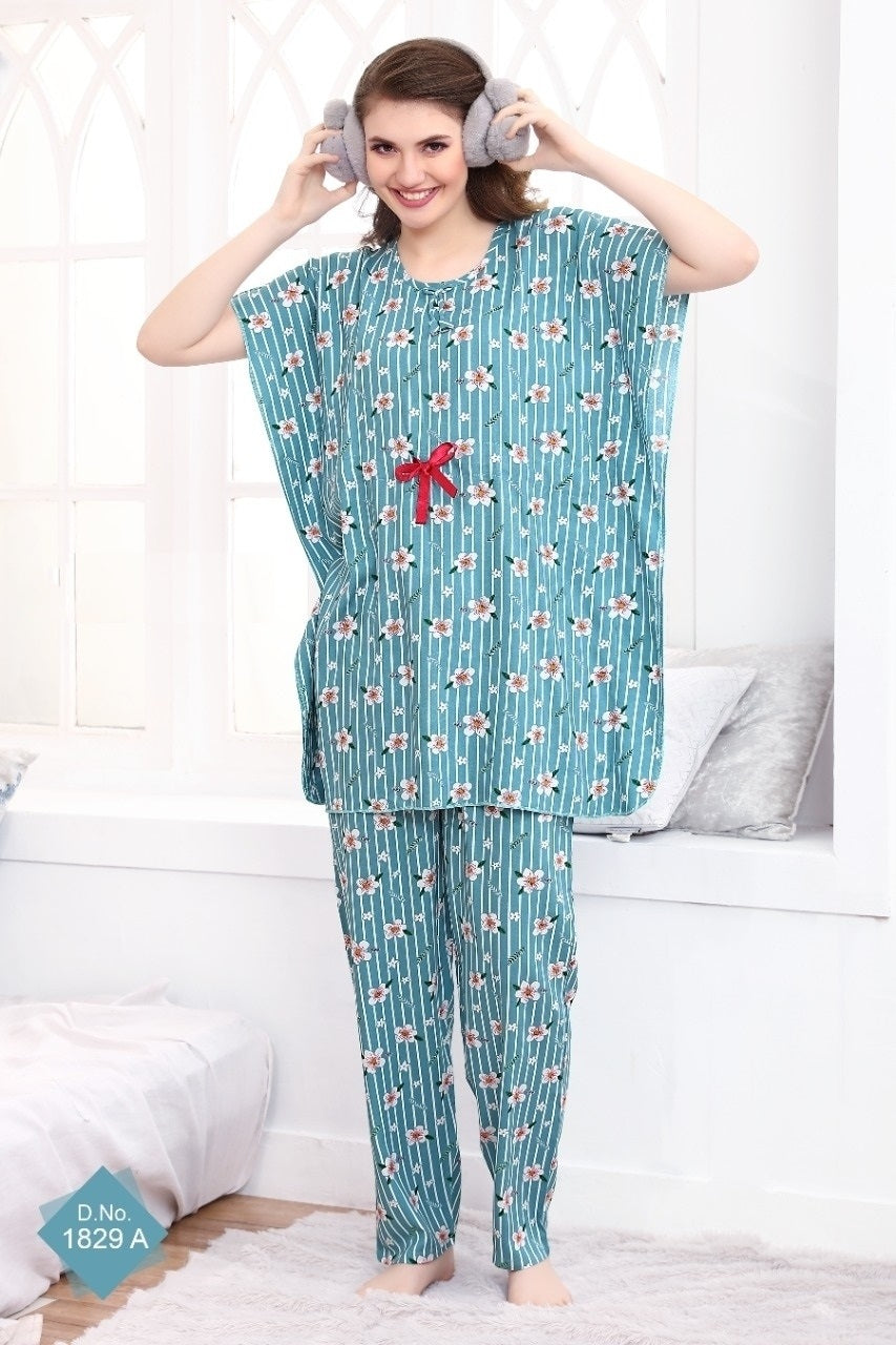 A woman wearing a blue floral print rayon kaftan night suit set with a drawstring waist and a pocket on the pants. She is indoors, standing, and posing with her hands raised to her head.