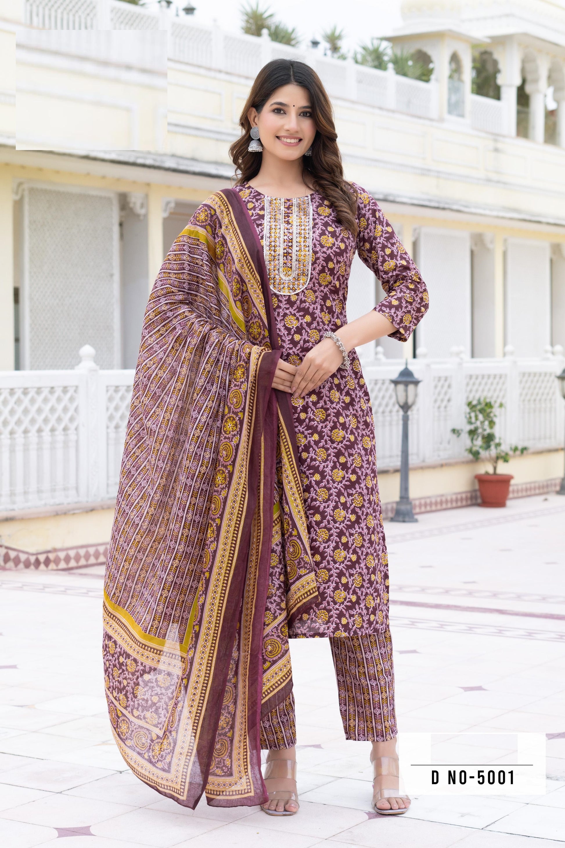 Woman wearing a traditional outfit with a purple and gold sari in front of a white building.